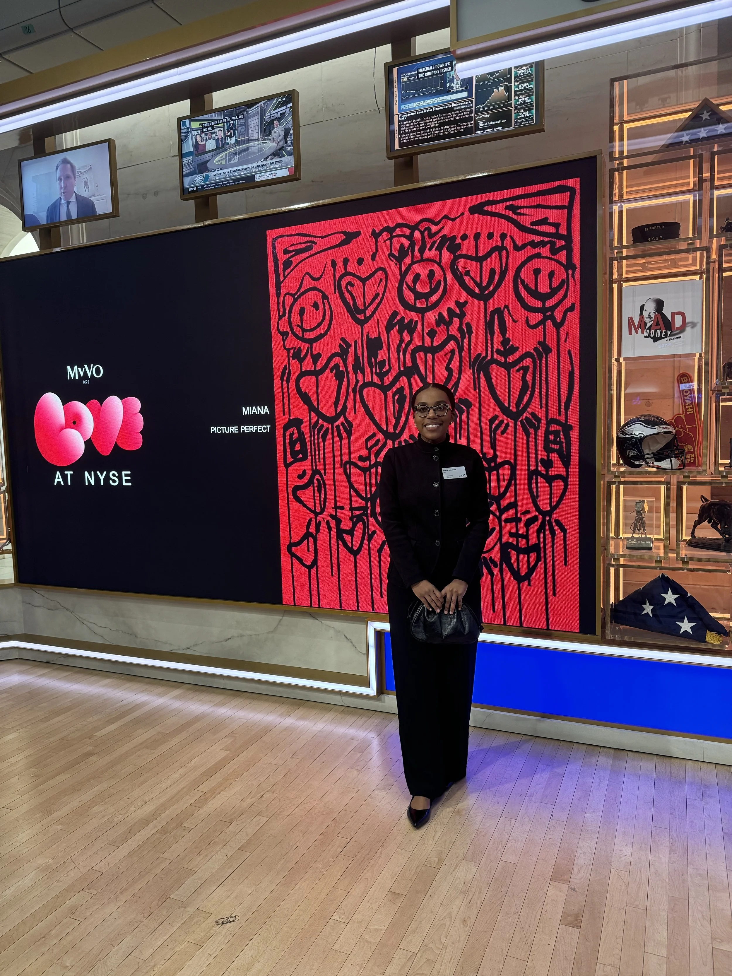 Visual artist, Miana, standing in front of her artwork on The New York Stock Exchange trading floor