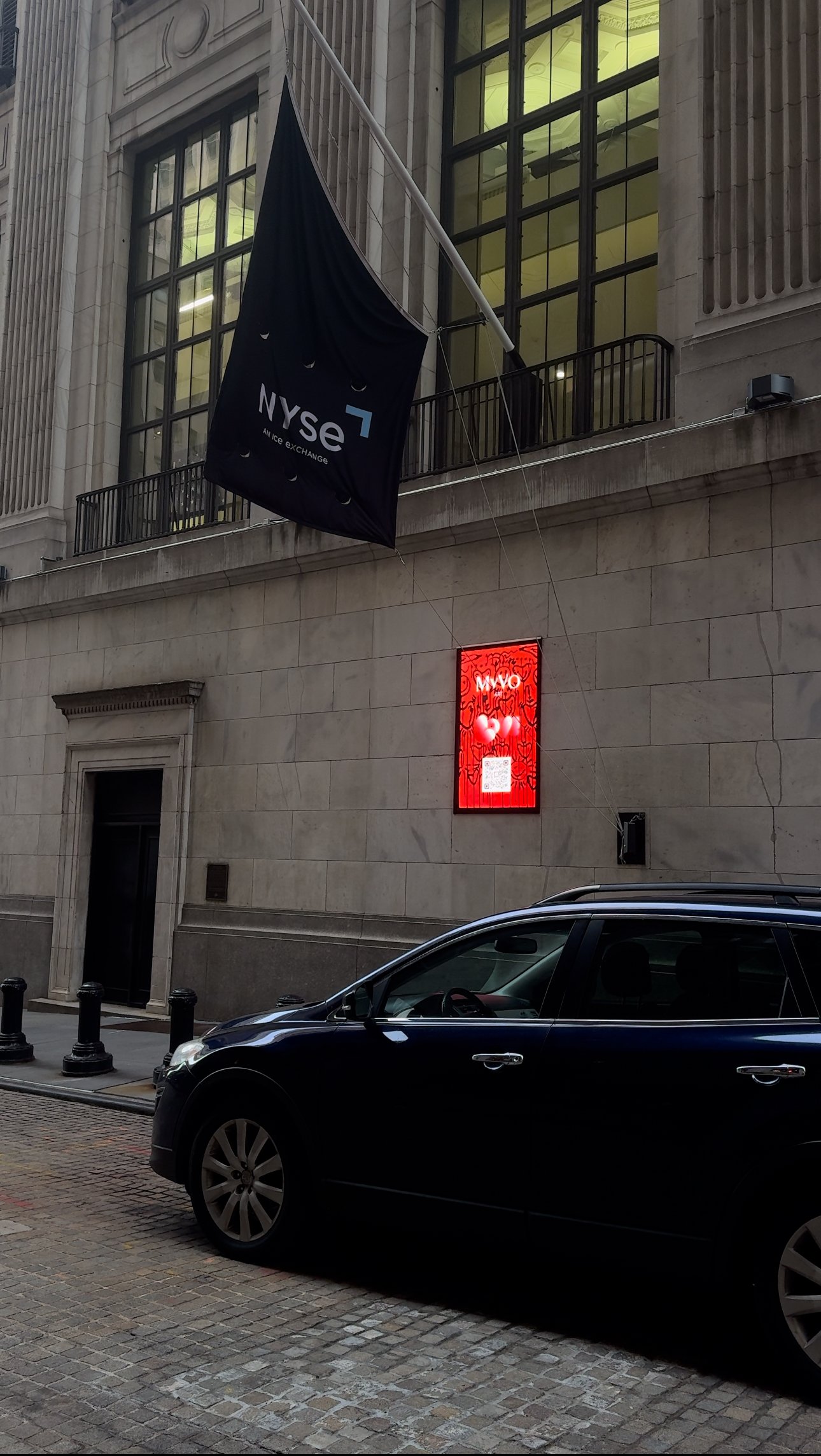 Visual artist, Miana, artwork featured on a screen outside of The New York Stock Exchange building beneath The New York Stock Exchange flag.