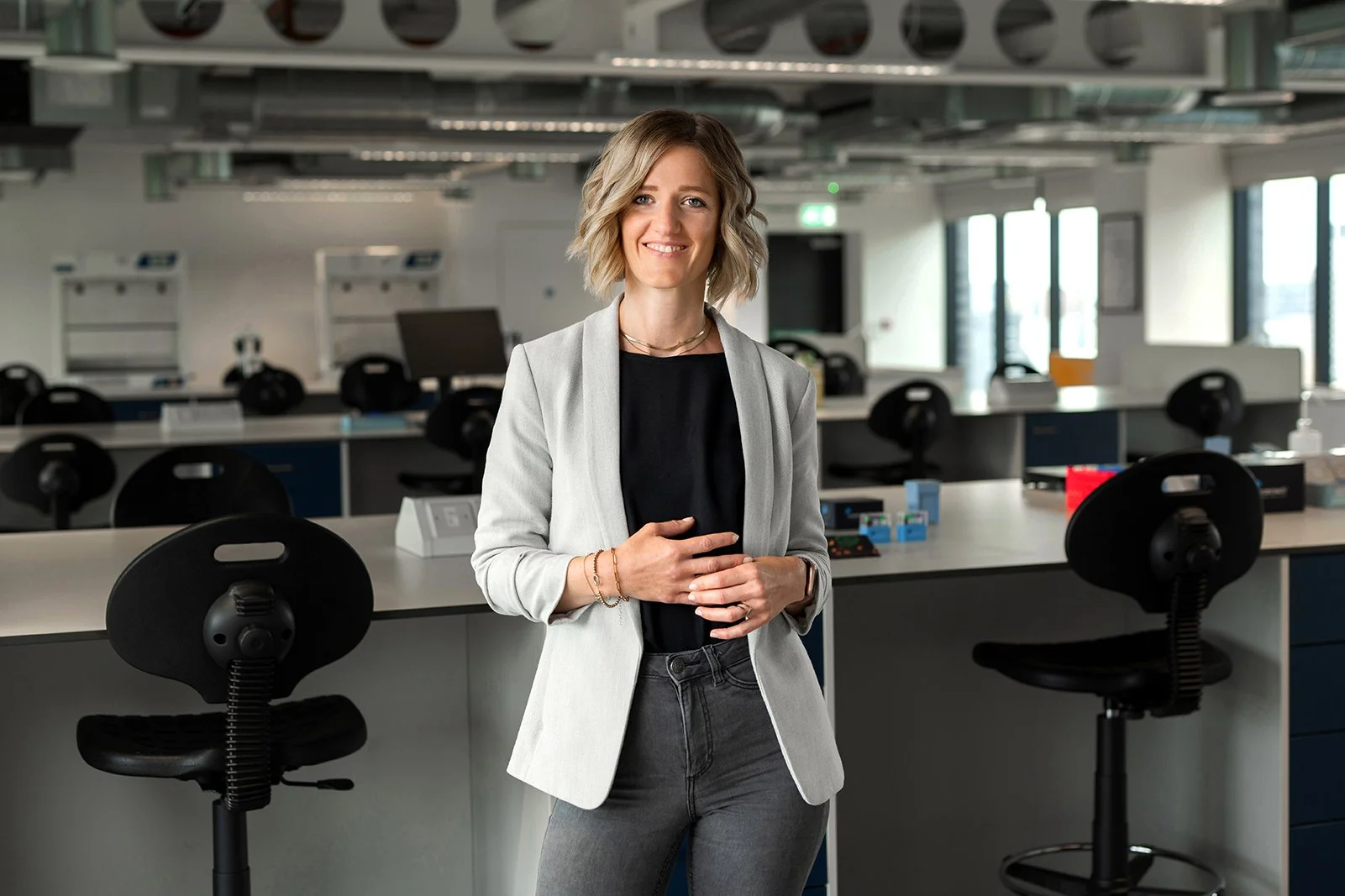 A woman standing in a modern office or laboratory space with workbenches and chairs around her.
