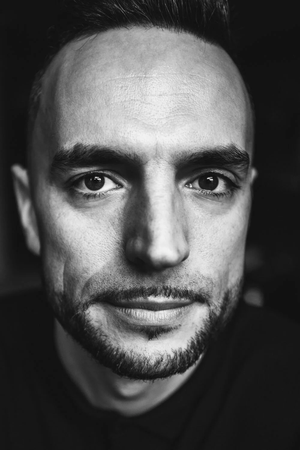 Black and white close-up portrait of a man with short hair, a beard, and expressive eyes.