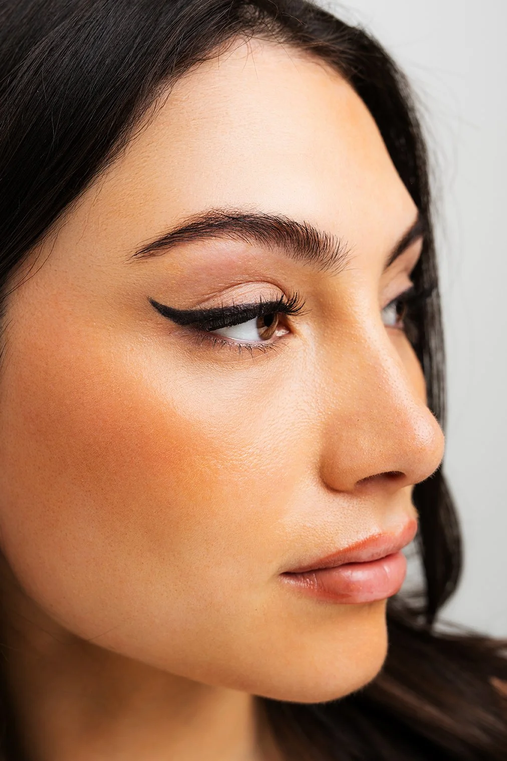Close-up of a woman's face showcasing makeup, including winged eyeliner, blush, and natural lip color.