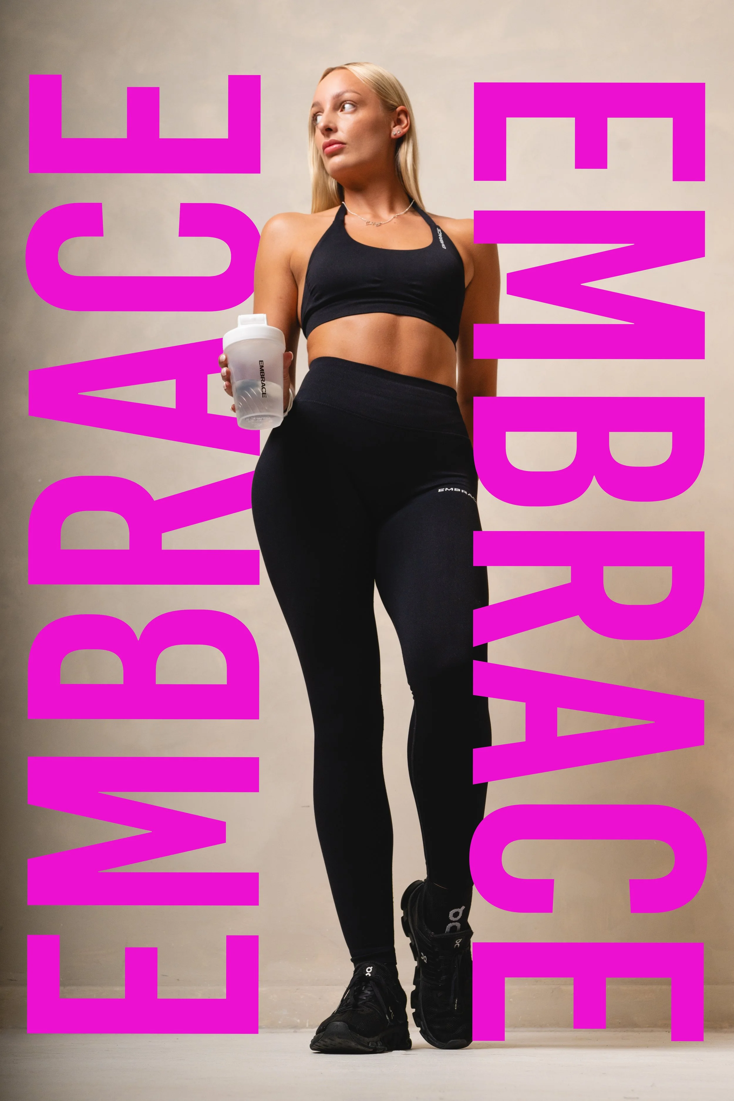 A woman in athletic clothing holding a water bottle, standing against a plain wall with bold pink text reading "BE WEALTHY" overlaying the image.