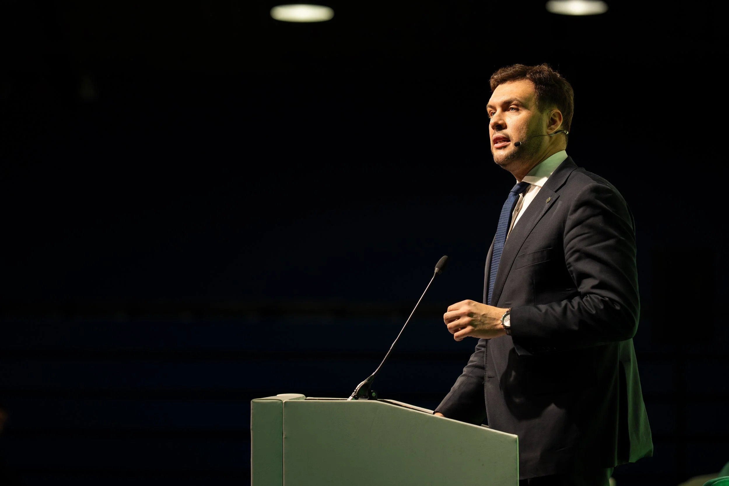 A man in a suit speaking at a podium with a microphone.
