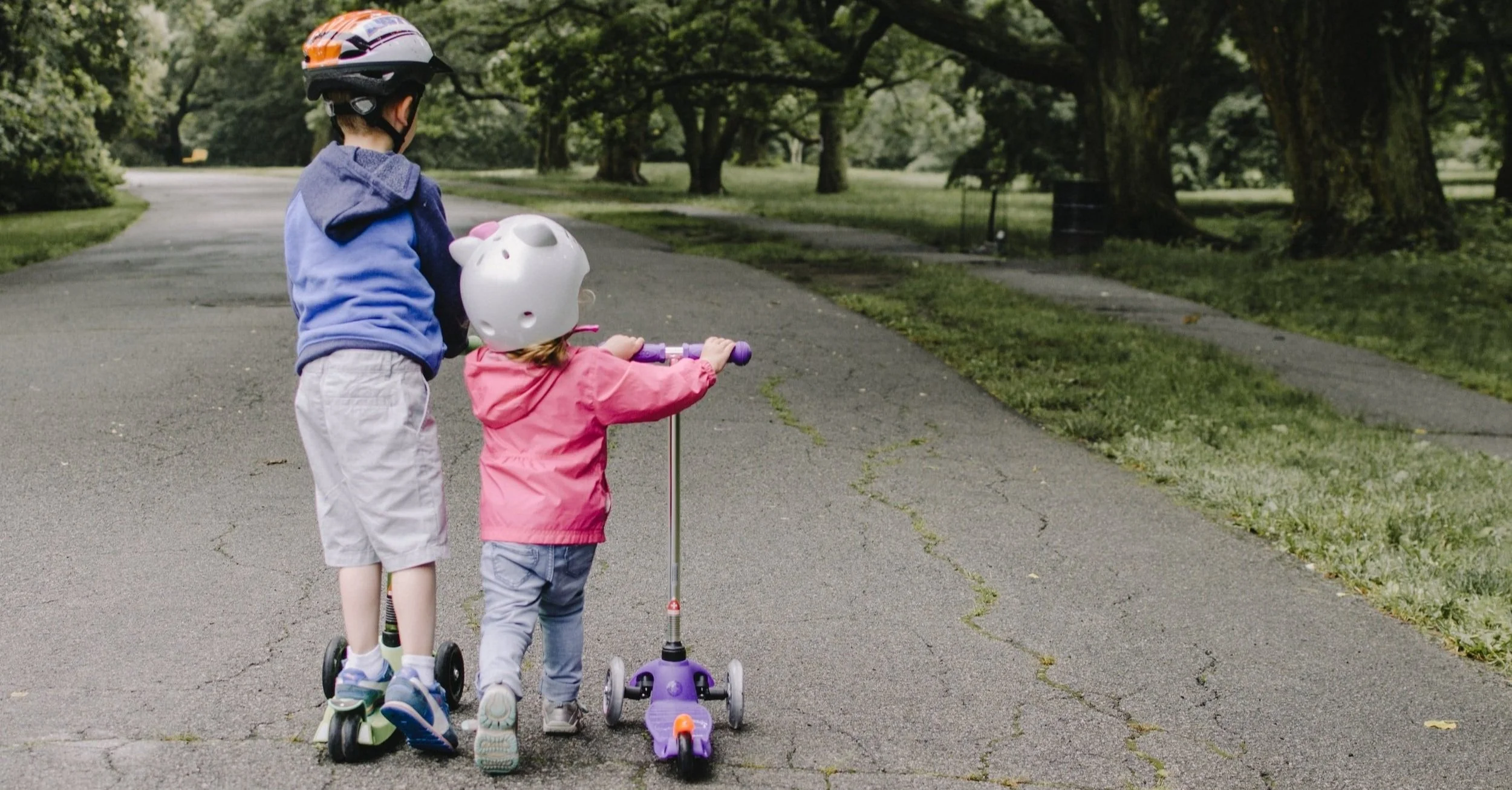 Two children on scooters down a park trail
