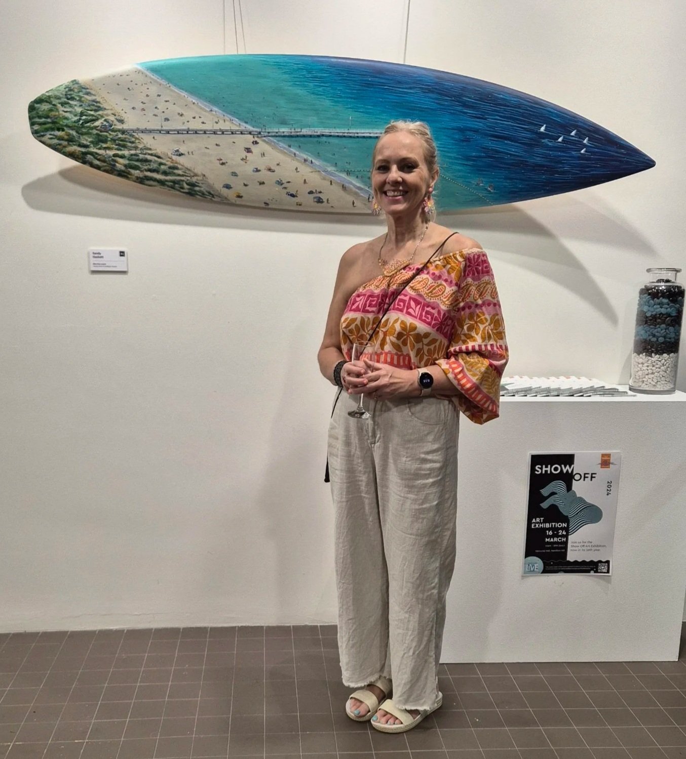Sandy Gaskett posing with surfboard artwork of Coogee Beach