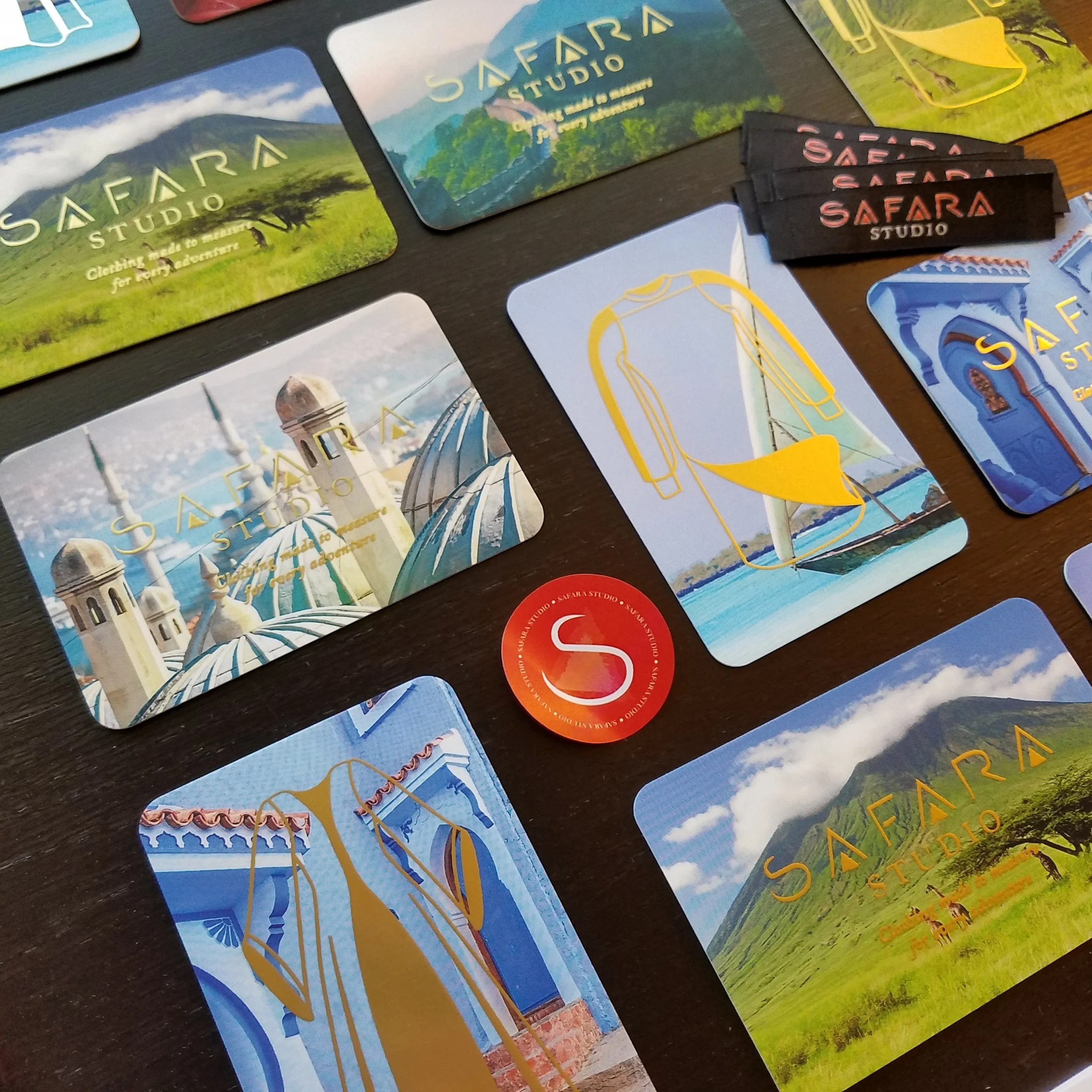 Collection of colorful cards and stickers featuring scenes of a mountain, lush greenery, Islamic architecture, and amusement parks, with the words 'SAFARA STUDIO' written on some of them.