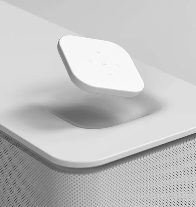 LJUD speaker with minimalistic controls hovering above a smooth surface, casting a slight shadow underneath.