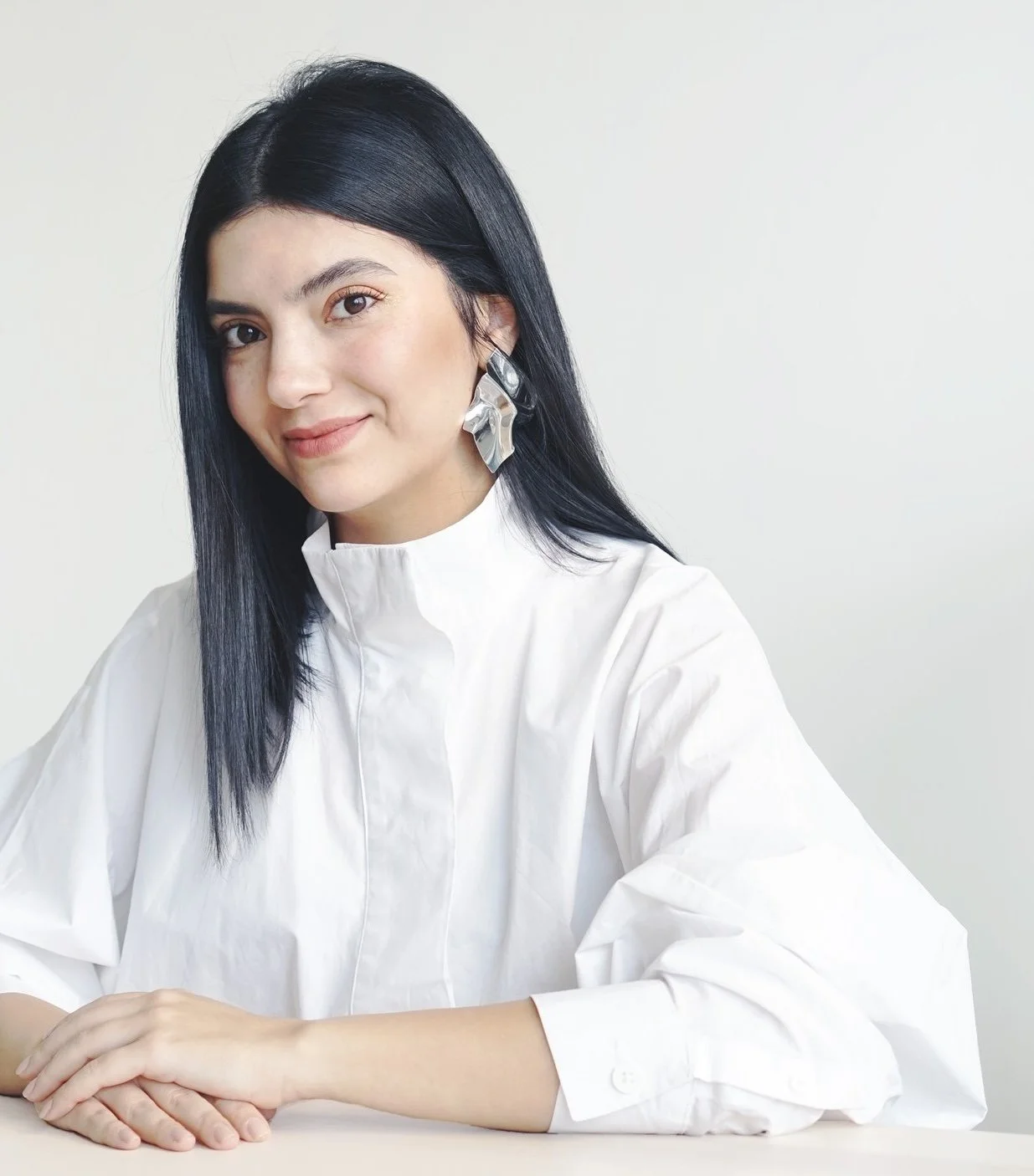 Fulden Dehneli sitting at a table with her hands resting on it, smiling at the camera. multi-award-winner turkish industrial designer