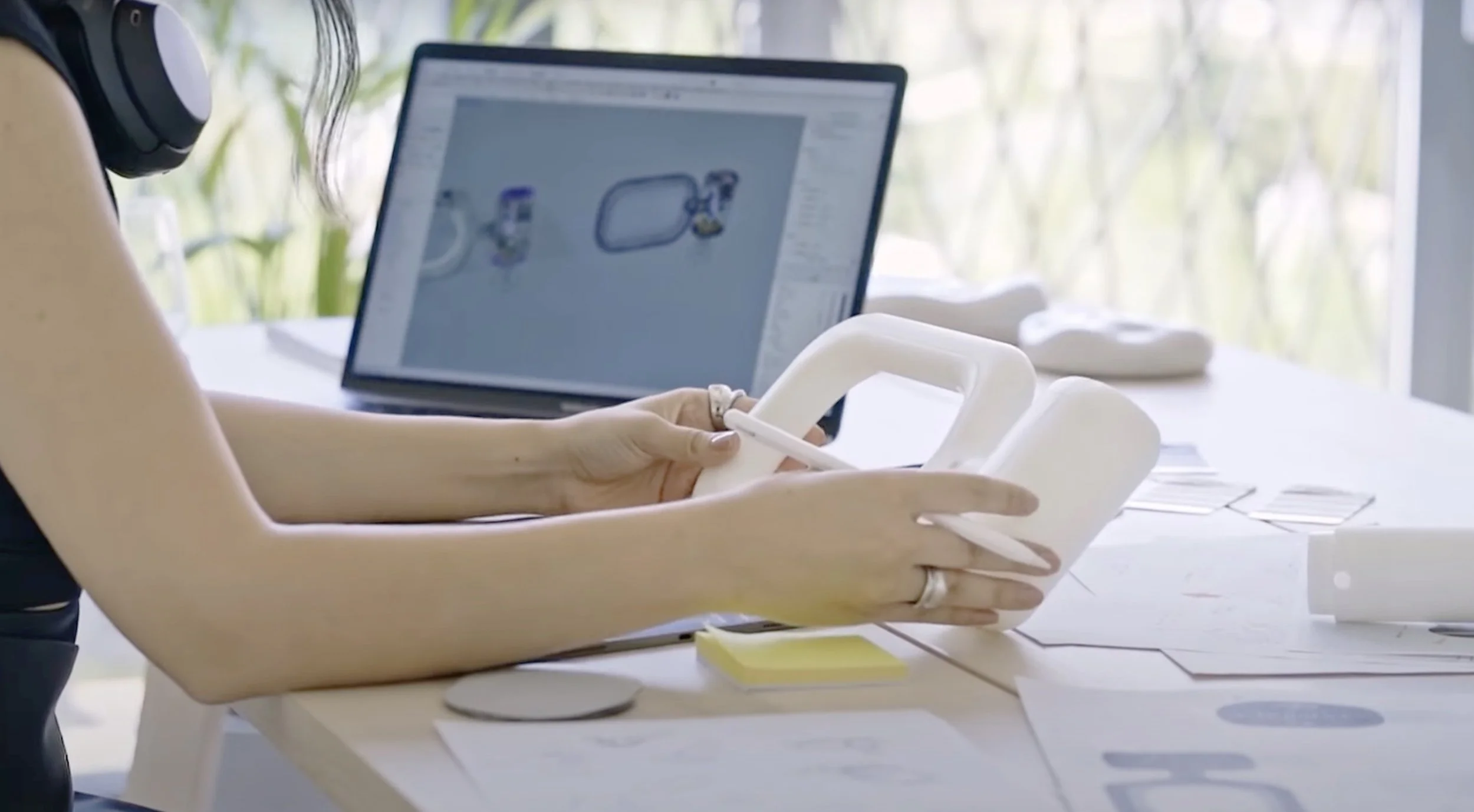 Fulden Dehneli working on a project with a computer, sitting at a desk with sketches, mockup and design materials, wearing headphones.