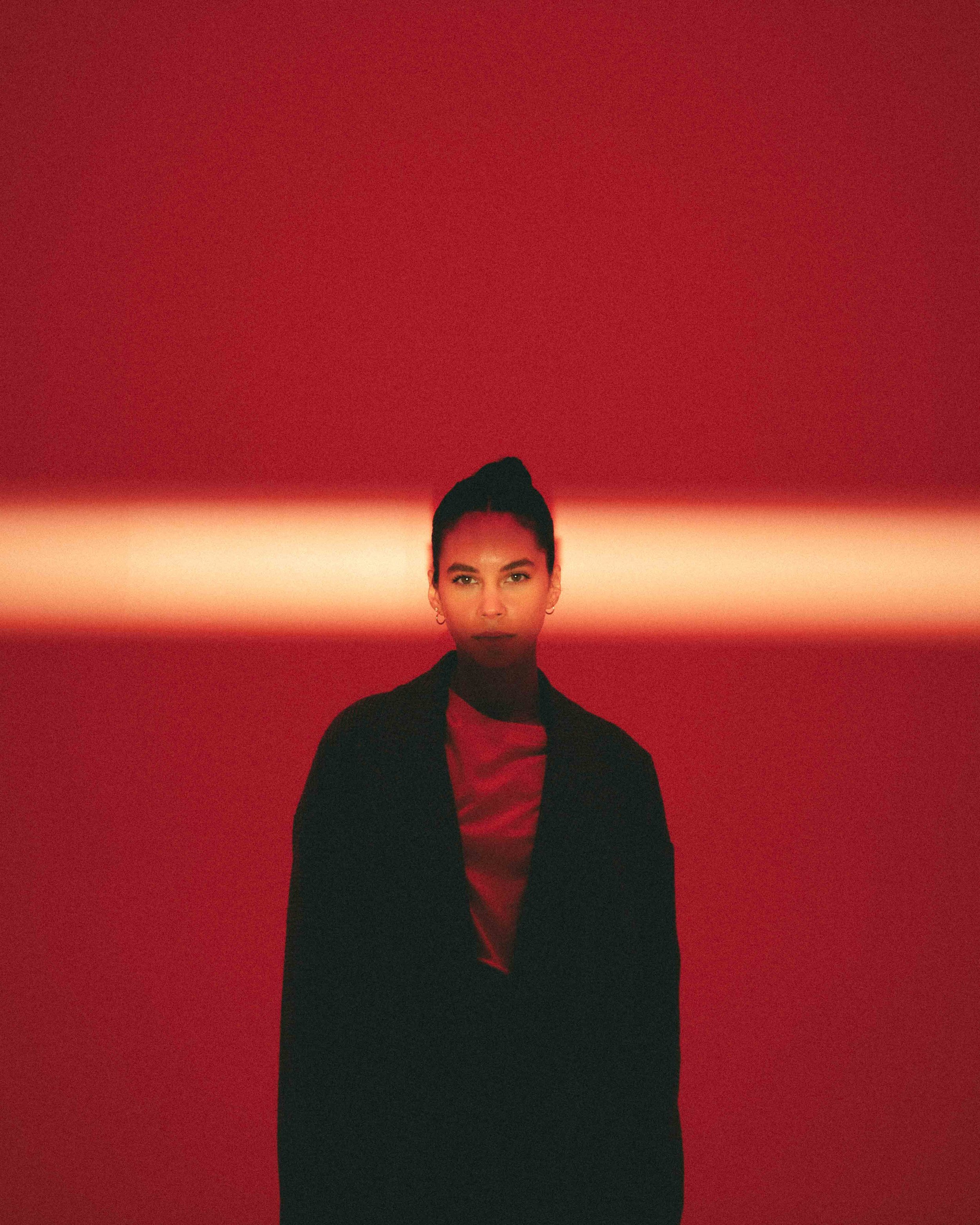 A woman standing against a red background with a horizontal red light streak across her face.