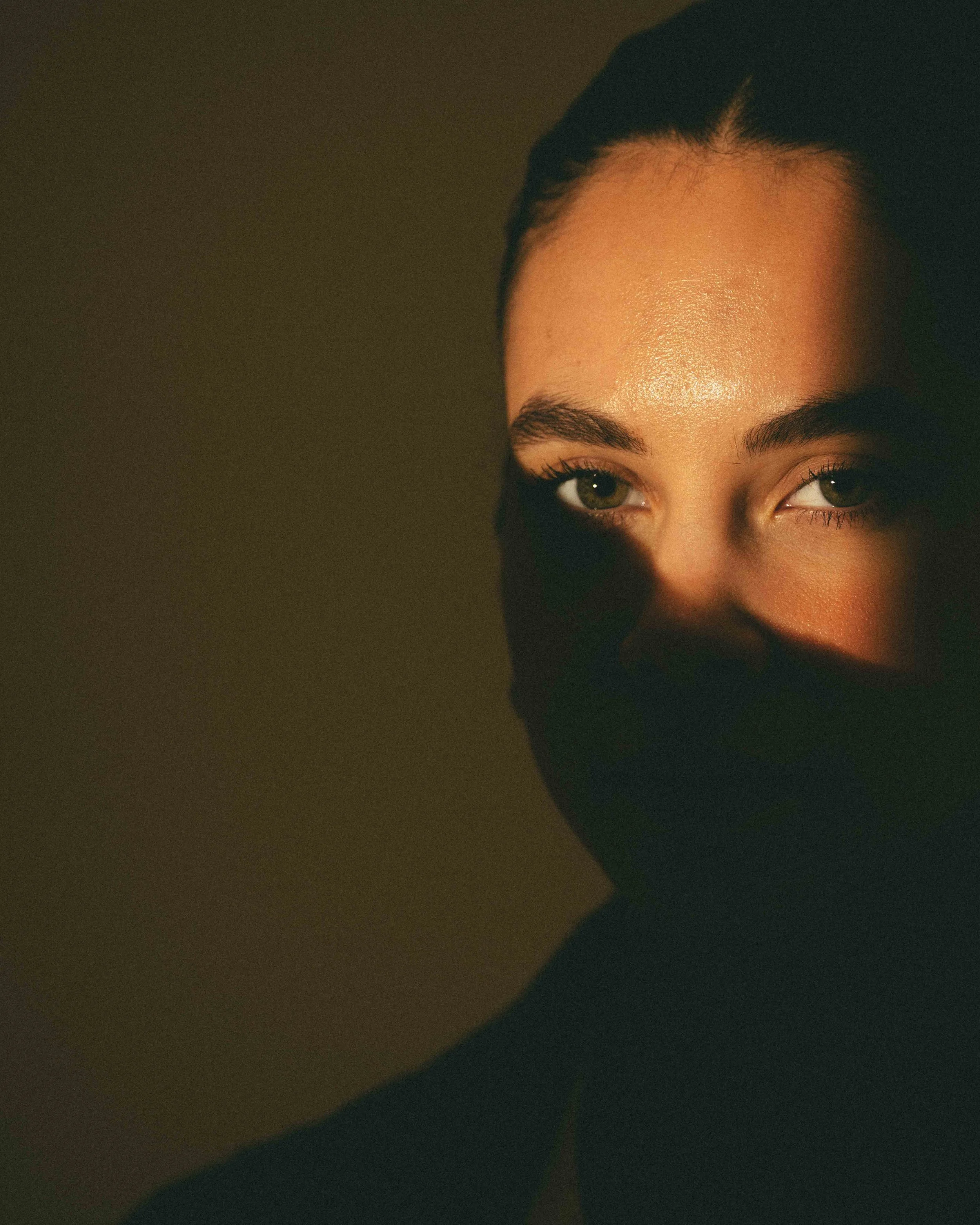 Close-up of a woman's face illuminated by warm light, showing her eyes and part of her nose, with a dark background.