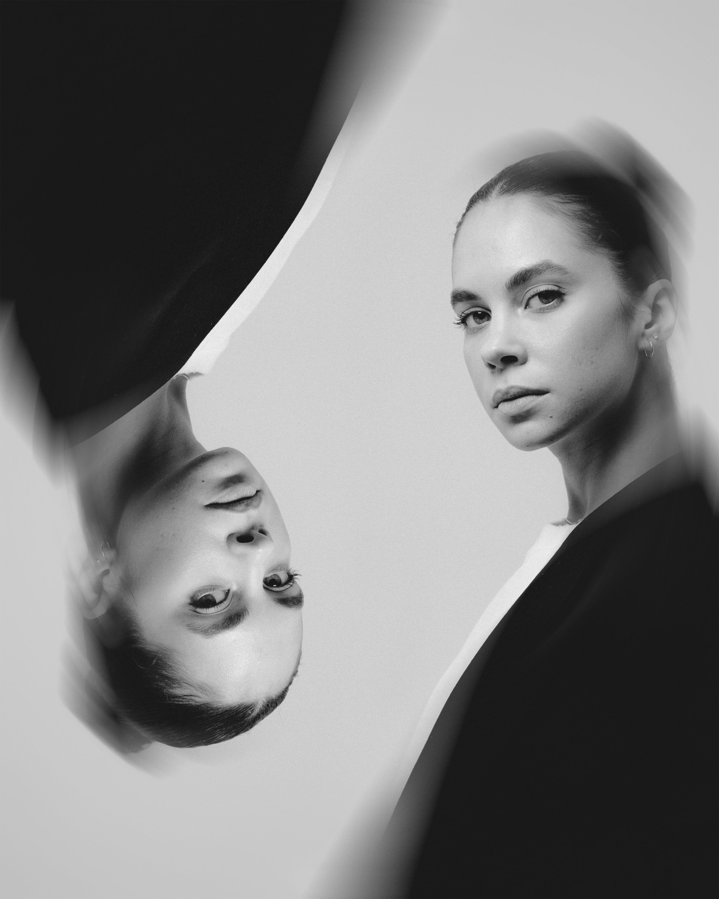 A woman with slicked-back hair looking directly at the camera, with her reflection visible in a mirror.