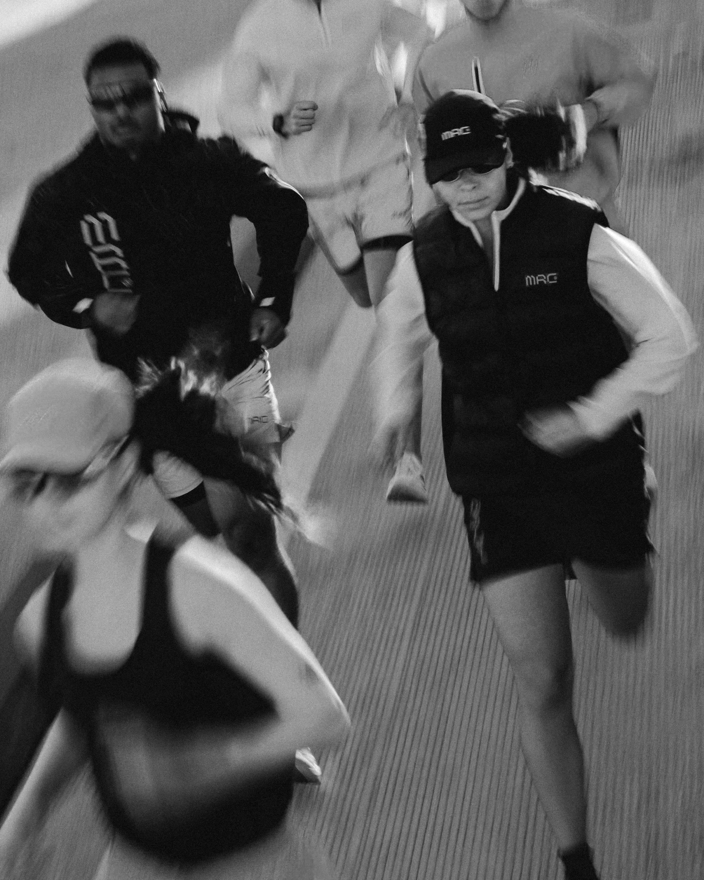 Group of people running indoors, some wearing sunglasses and athletic clothing, possibly participating in a race or fitness event.