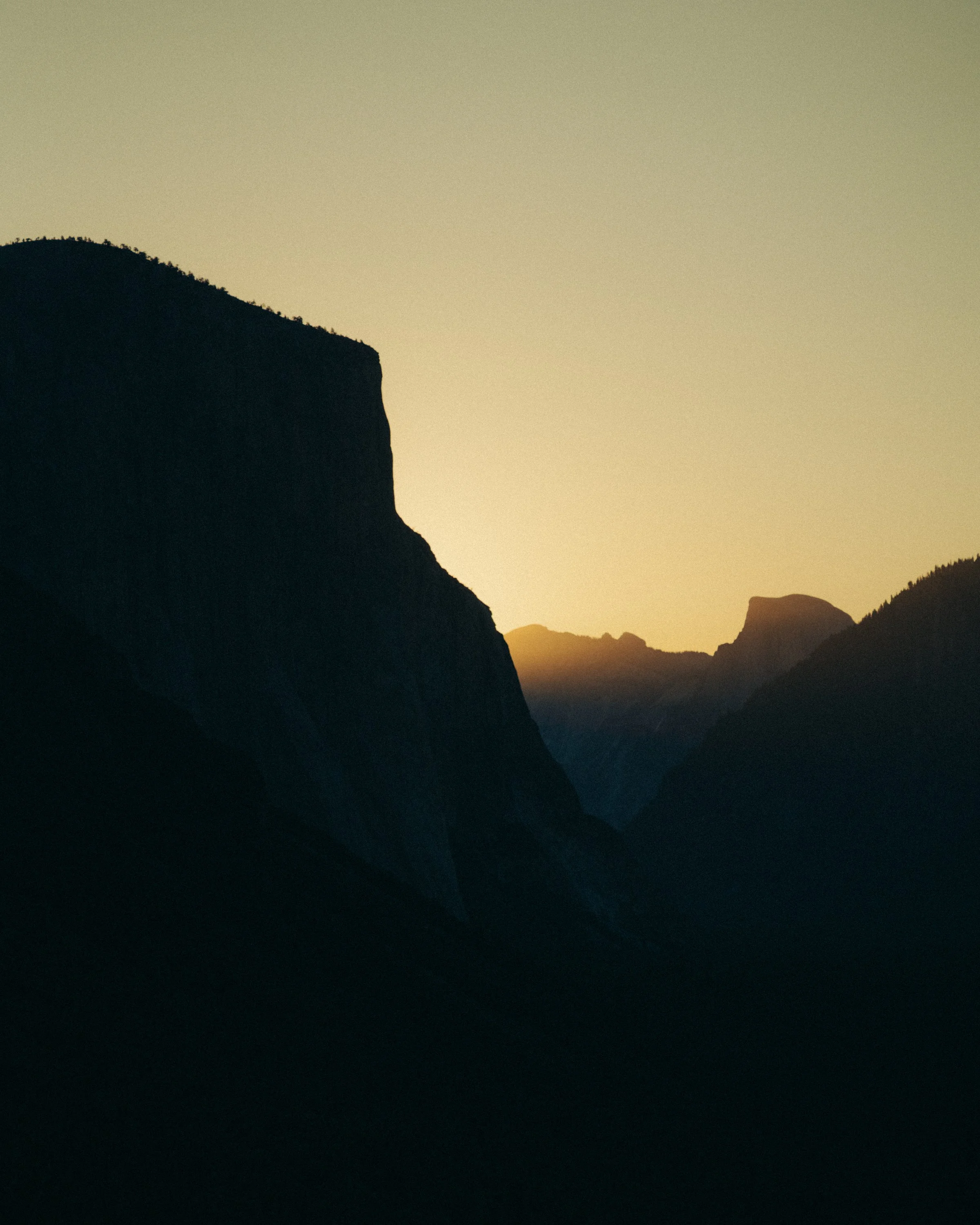 Silhouettes of cliffs and mountains during sunset or sunrise with a gradient sky in the background.