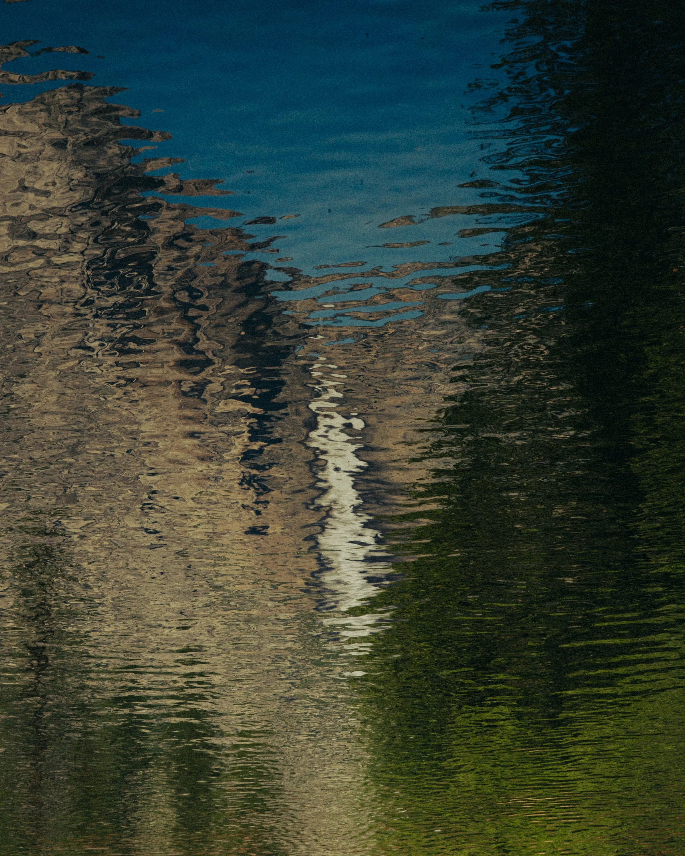A reflection of a building and trees on a body of water, creating a distorted mirror image with ripples.