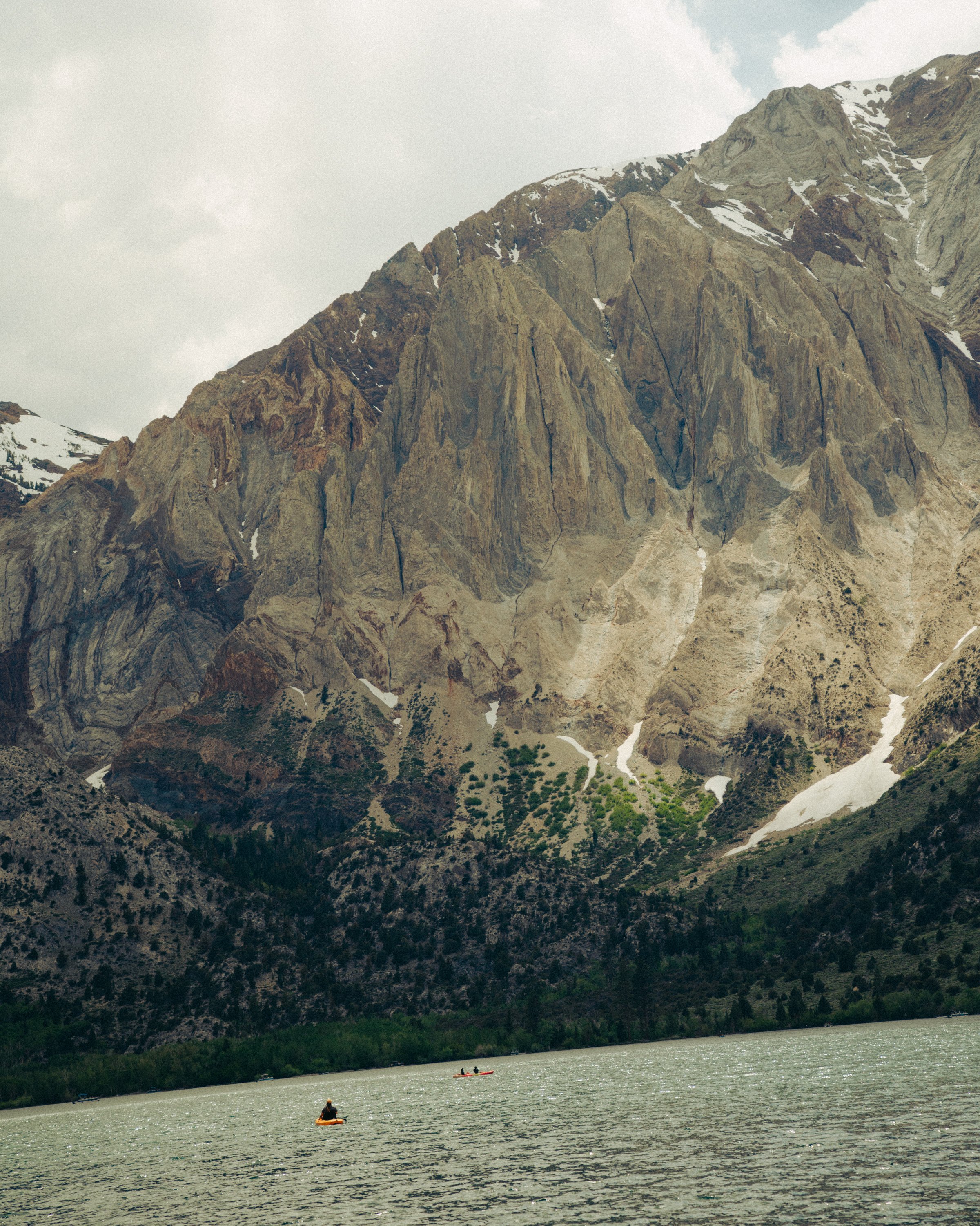 People kayaking on a river with high rocky mountains with patches of snow in the background.