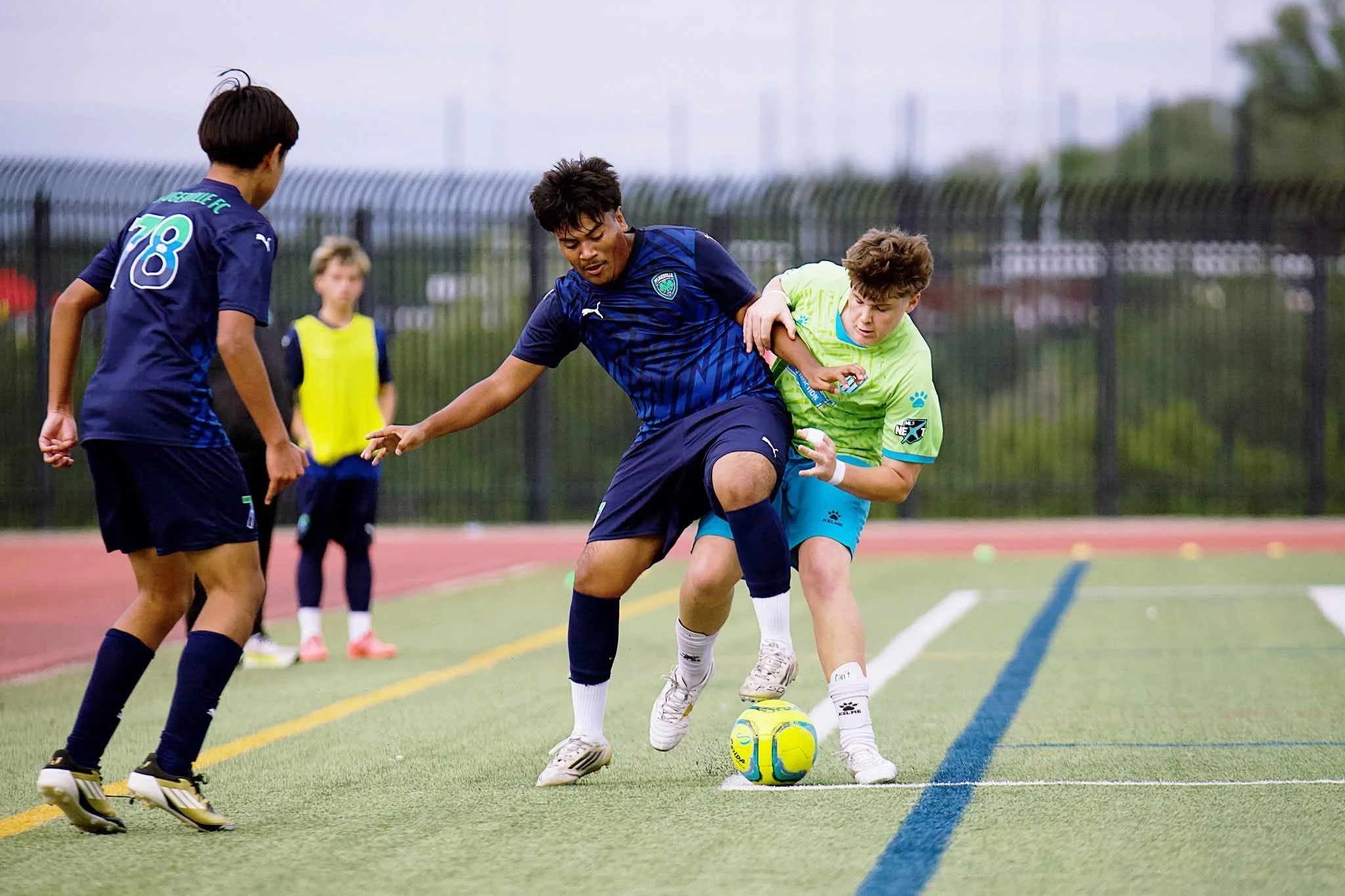 A female soccer player in a green jersey with the name 'PFLUGER' and number 13, standing on a soccer field at night, with other players and spectators in the background.