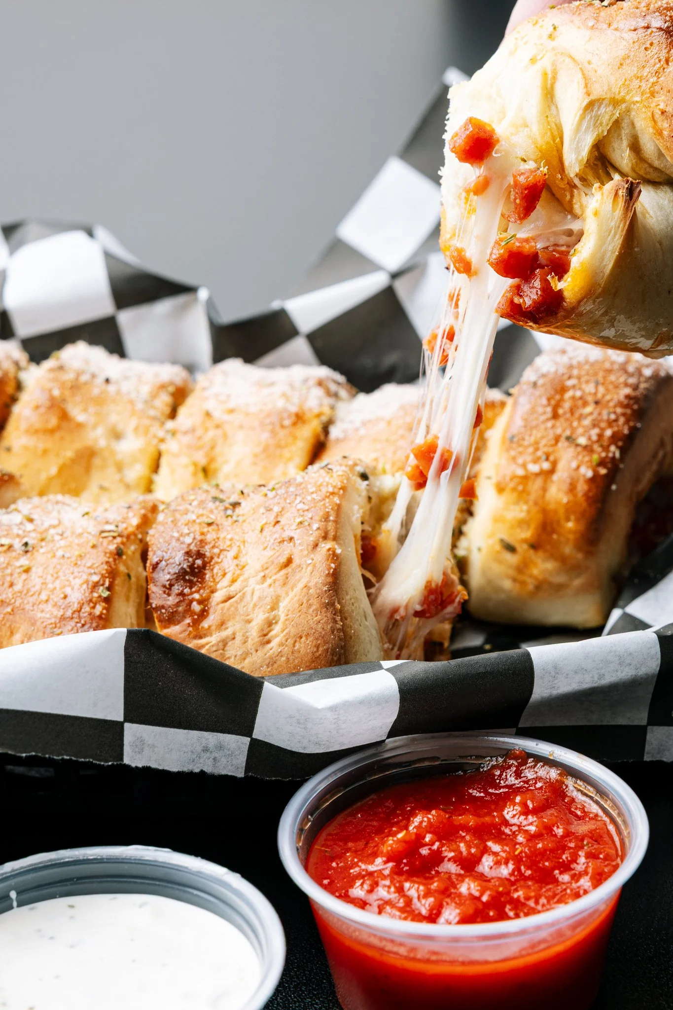 Fried mozzarella sticks topped with marinara sauce, with small containers of ranch and marinara sauce in the foreground.