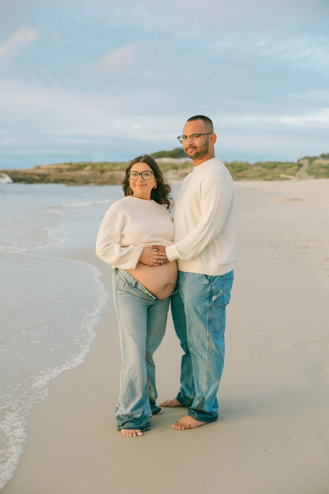 A pregnant woman and her partner standing by the soft ocean waves during a Tampa, FL maternity session.