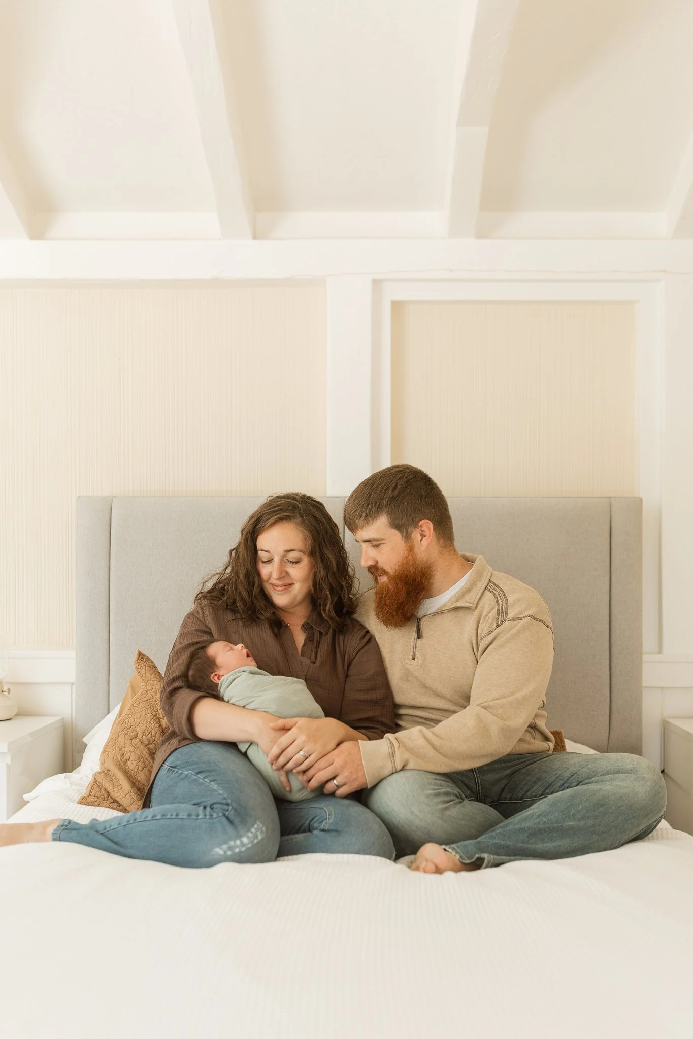 Mom and dad sitting on their bed holding their newborn baby during an at-home newborn session in Tampa, FL.