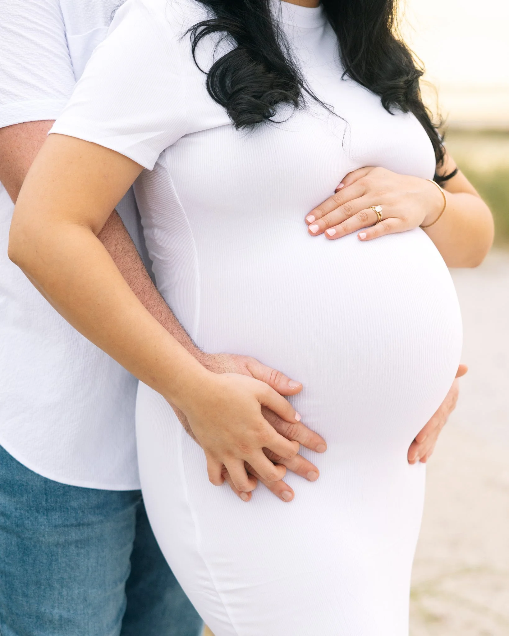 A close up image of an expectant mother's belly with her hands and her husbands hands wrapped around each other.