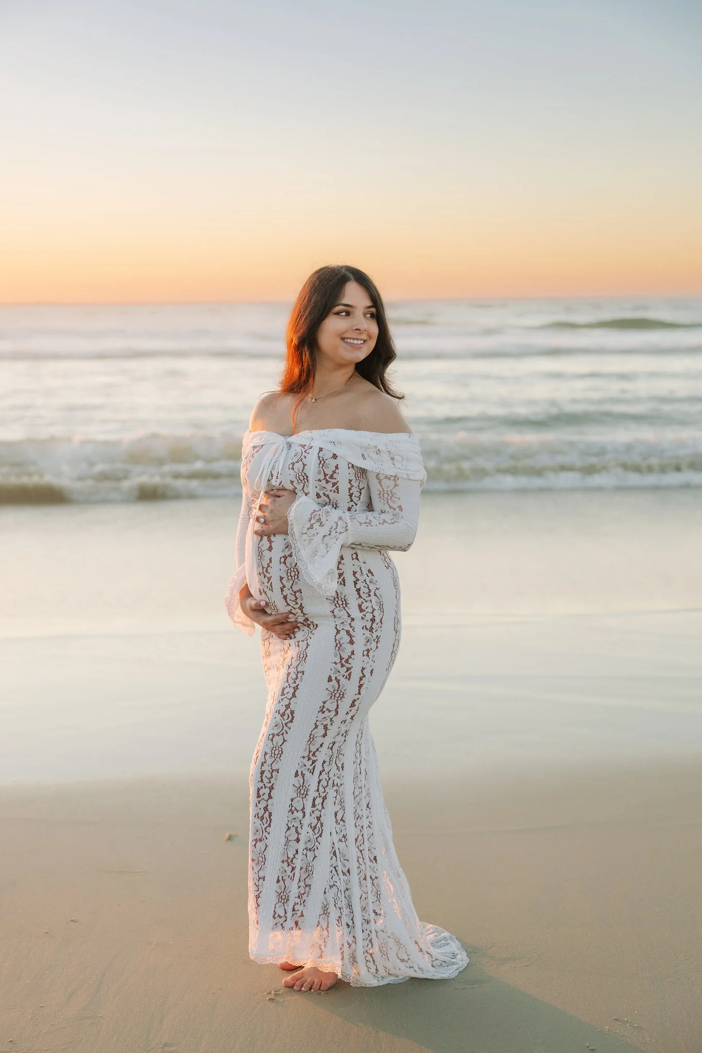 Pregnant woman standing on the beach with waves rushing in behind her as she poses for a Tampa maternity photo.