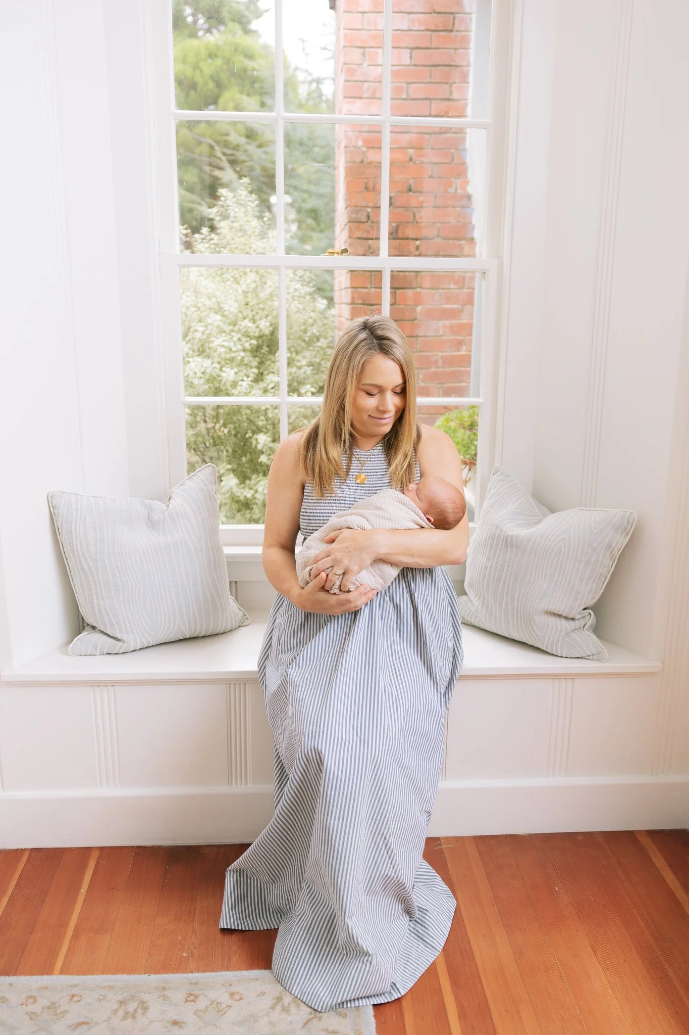 A mother cradling her newborn baby while sitting at a window in her home during a Tampa, FL at-home newborn session