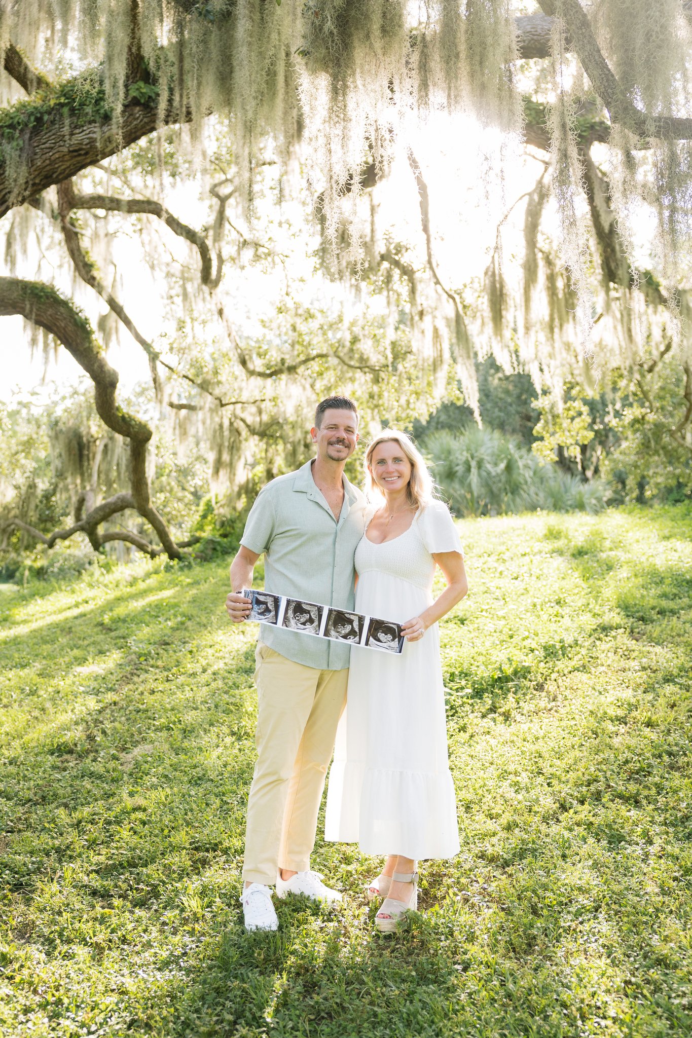 Couple holding an ultrasound strip beneath a sprawling live oak draped in Spanish moss at Philippe Park, Safety Harbor FL