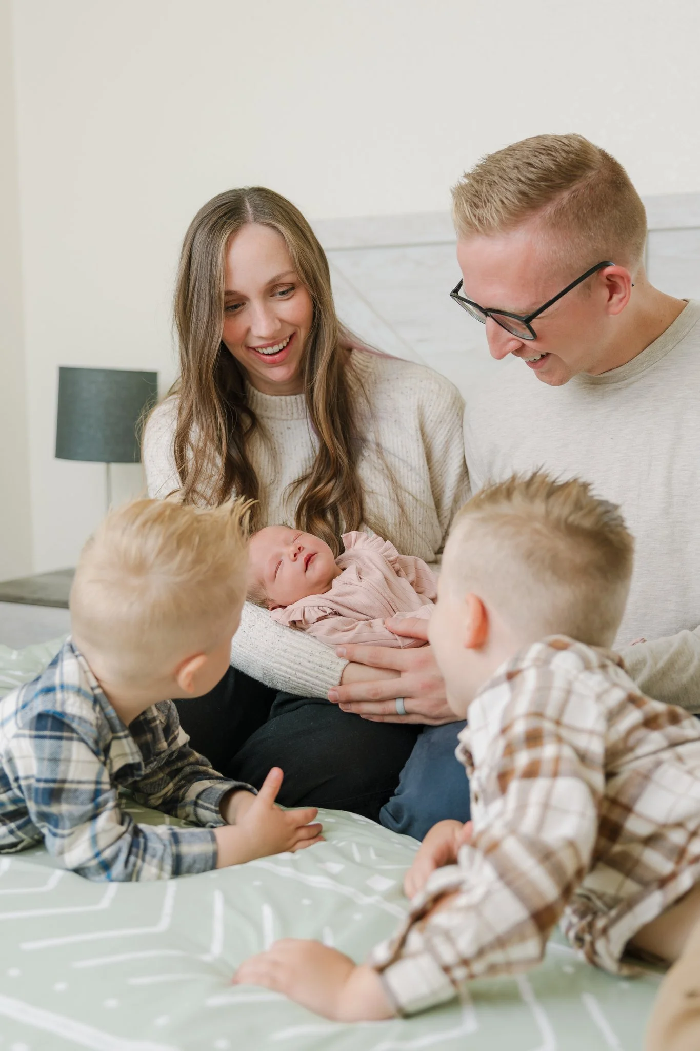 Mom, dad, and toddler siblings admiring newborn baby on their bed during a Tampa, FL at-home newborn session.