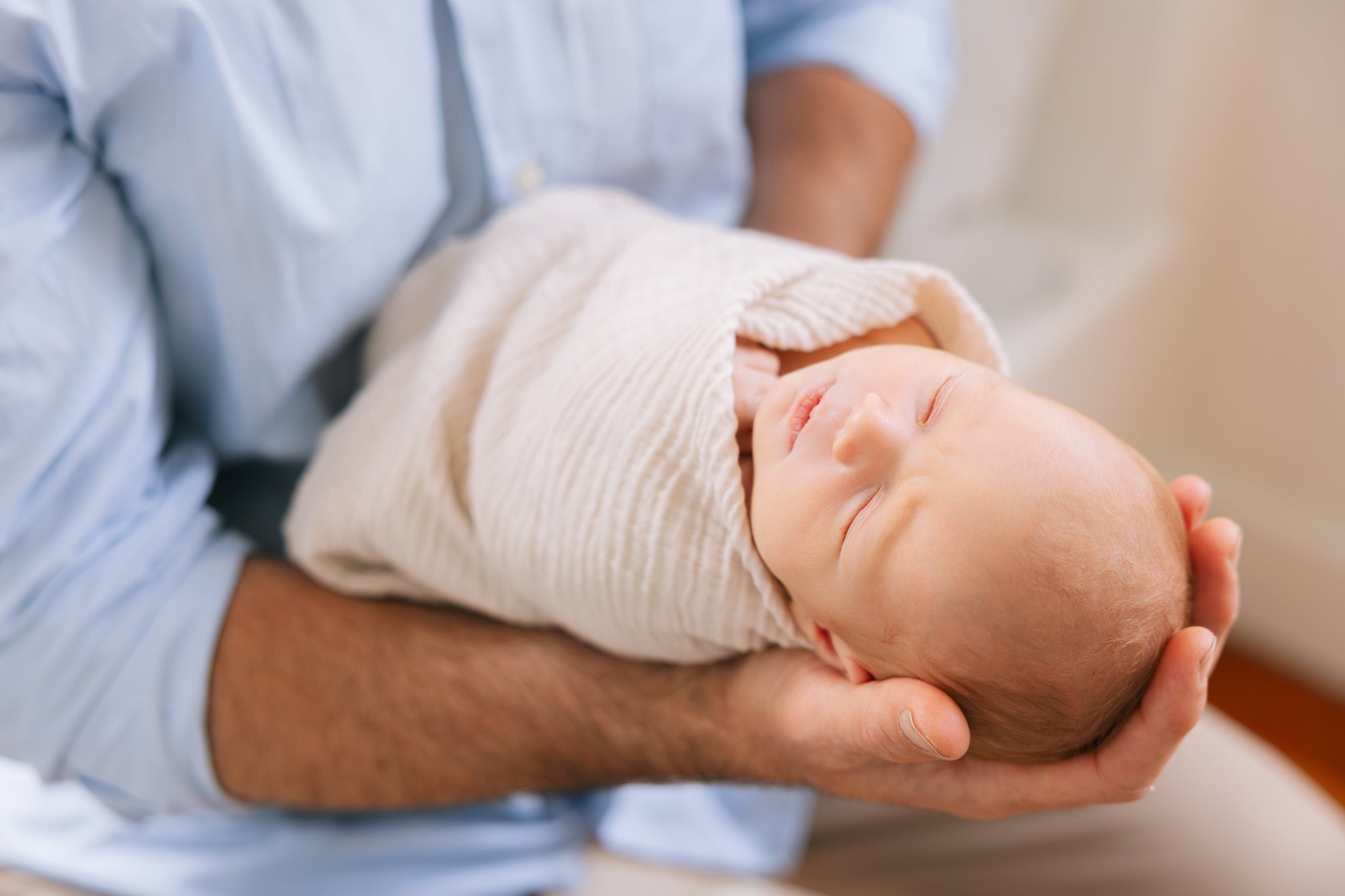 Close up of a father holding his newborn baby swaddling in a cream swaddle during an at-home newborn session in Tampa, FL.