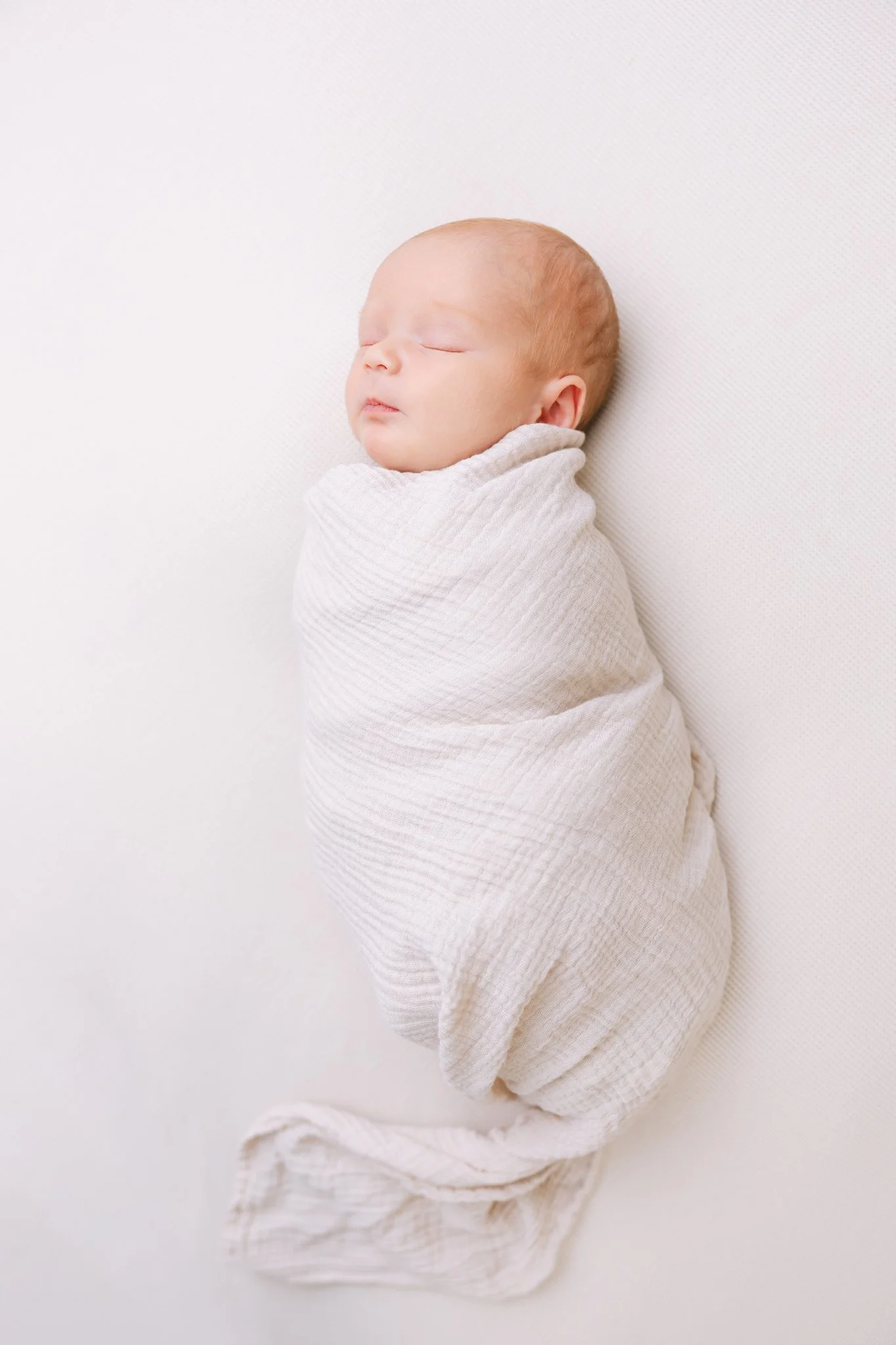 Newborn swaddled in cream wrap, sleeping, during an at-home newborn session in Tampa, FL.