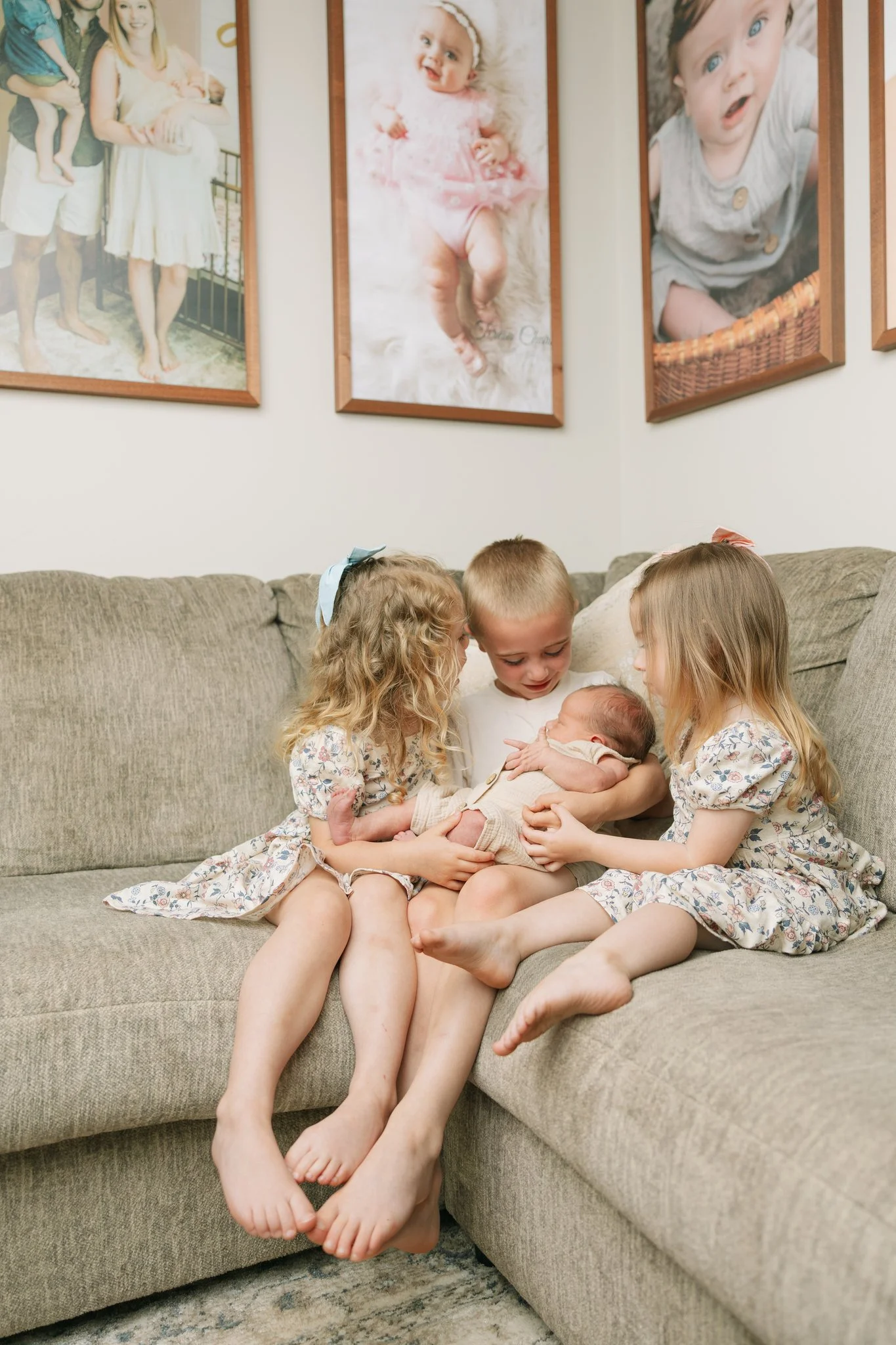 3 siblings sitting on a couch together at home, holding their newborn baby brother, for a photo during an at-home newborn session.