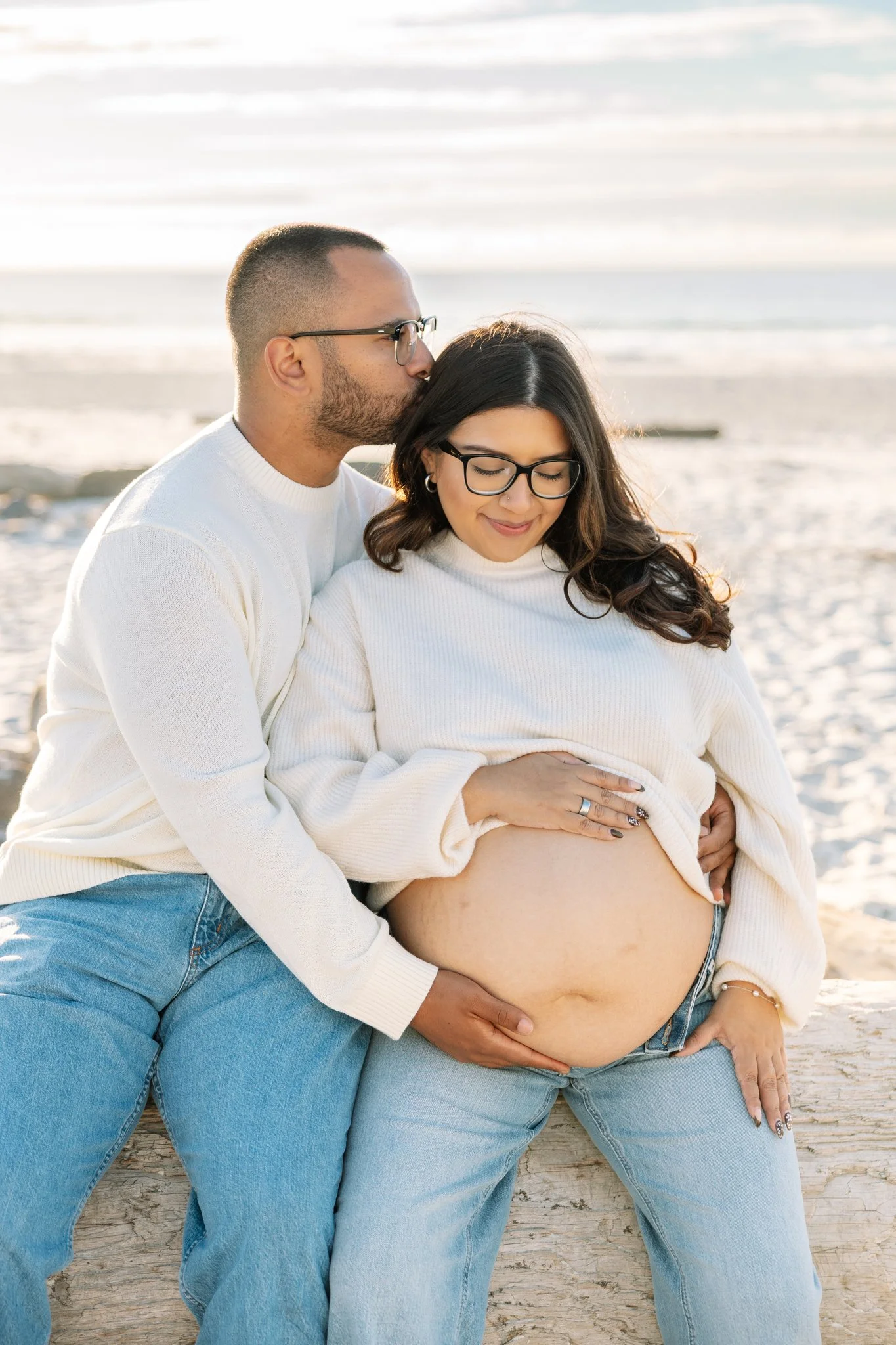 Couple sitting together on driftwood on the beach posing for beach maternity photos in Tampa, FL.