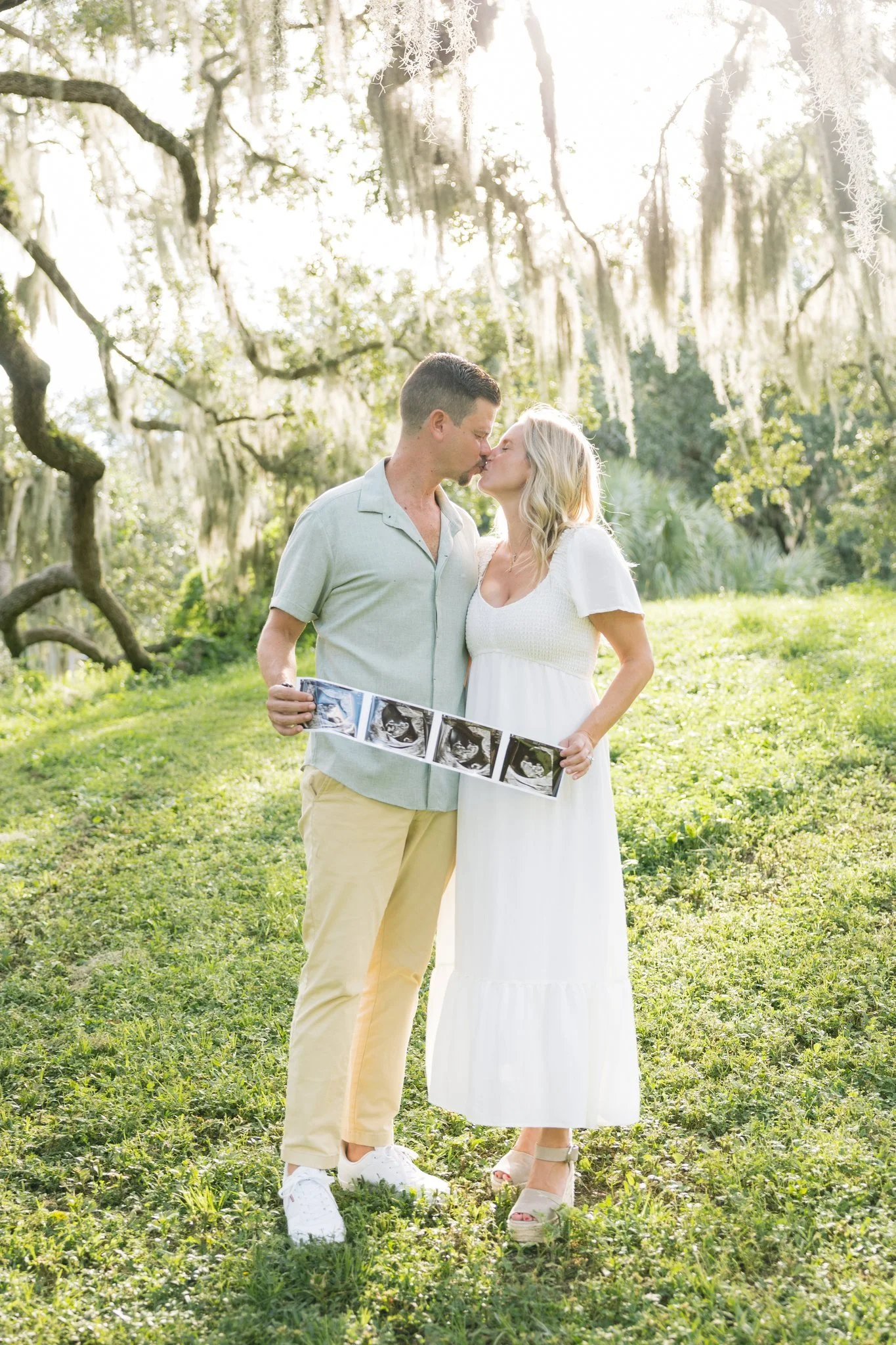 Couple sharing a kiss while holding an ultrasound strip under moss-draped oaks in Safety Harbor, Florida