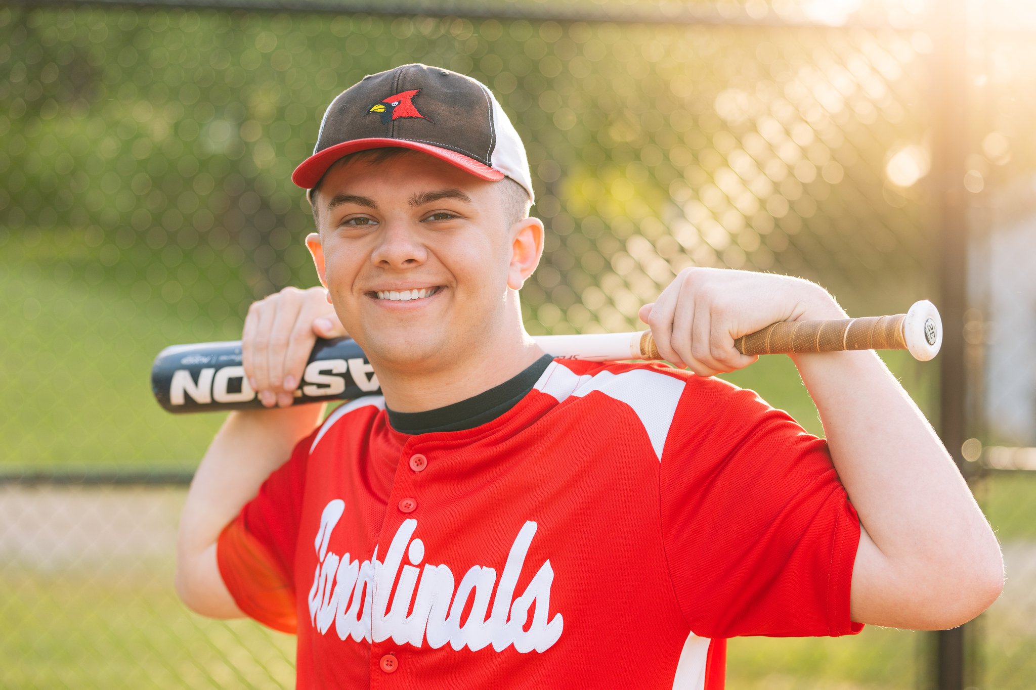 A male graduate posing for a senior photo session in Tampa, FL in his baseball uniform and holding his bat.