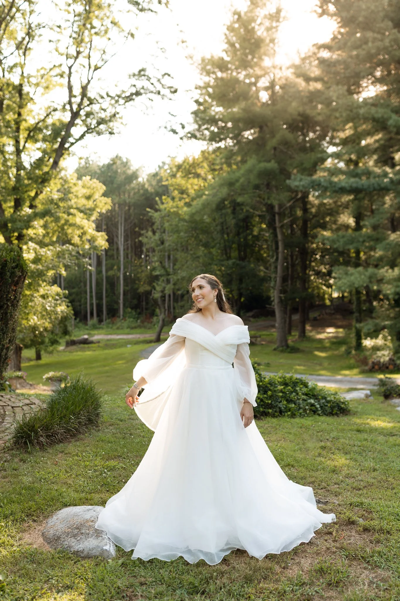 A bride standing outdoors in green grass, twirling in her wedding dress.