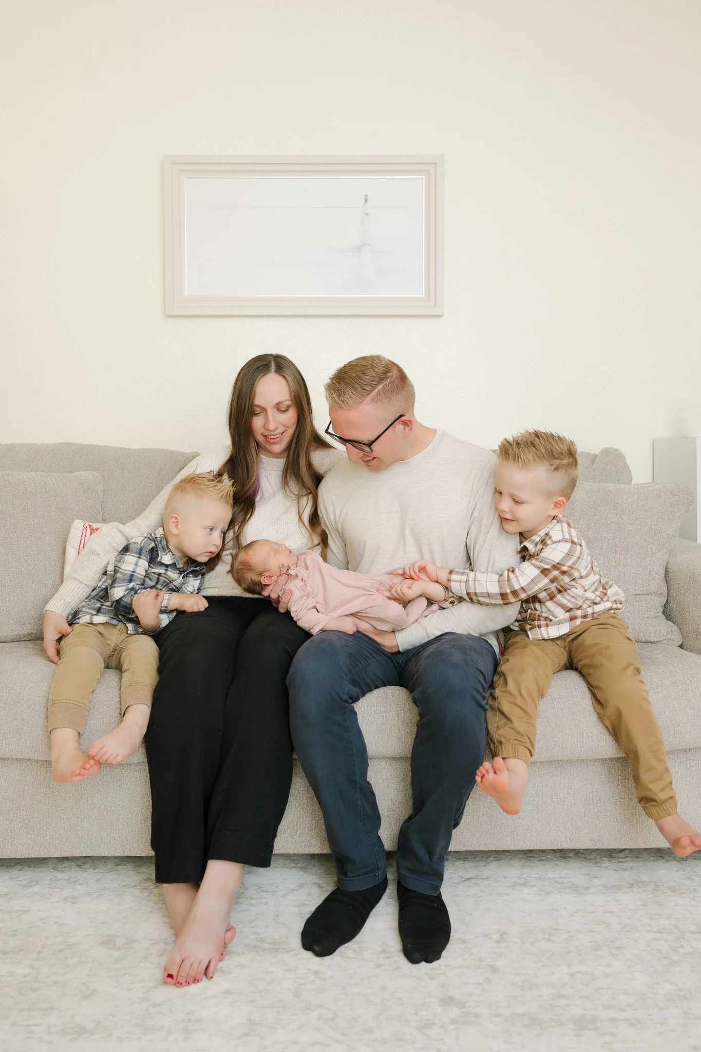 Mom and dad holding their newborn baby with toddler siblings on the couch in their home during a Tampa, FL at-home newborn session