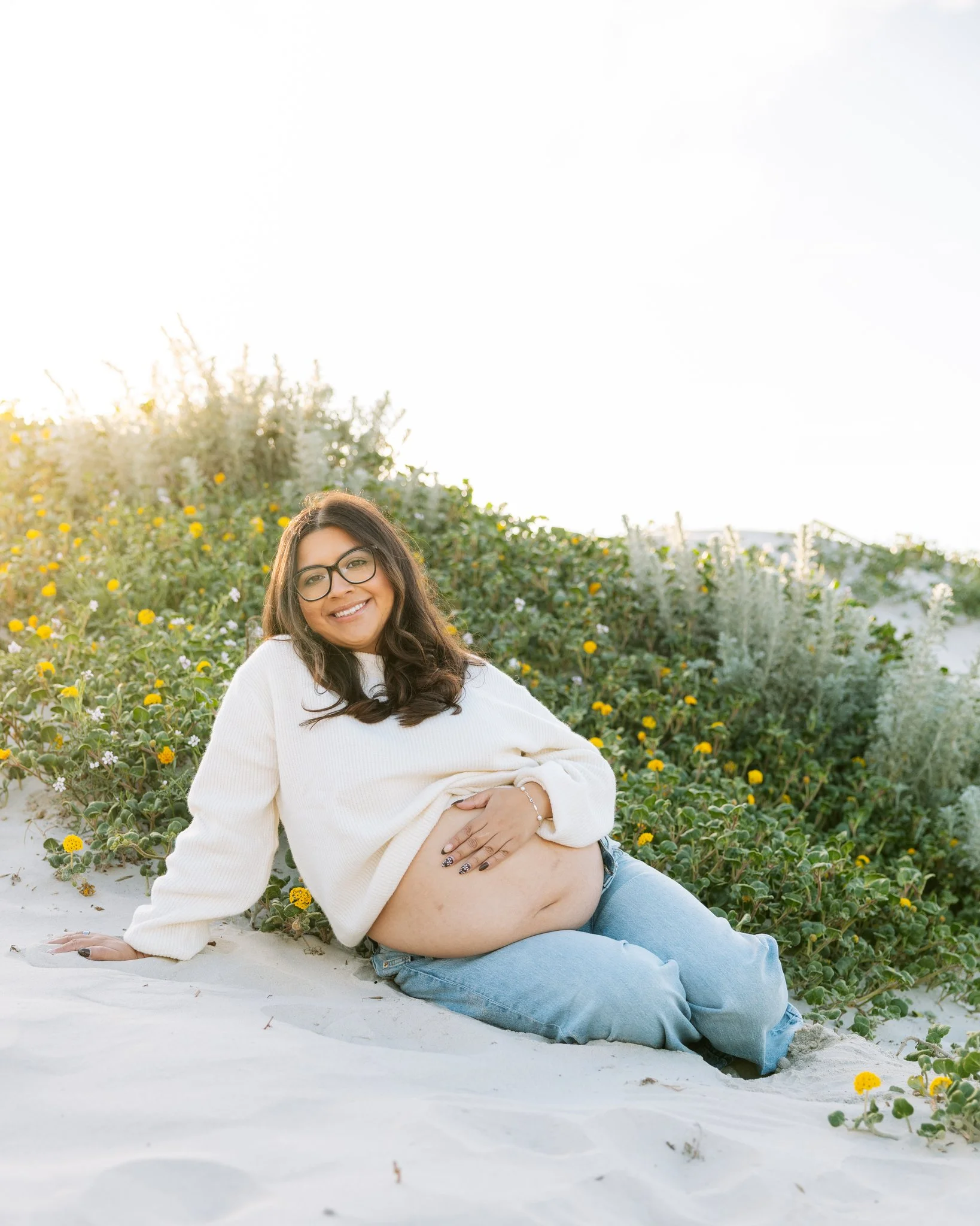 Pregnant woman sitting on beach and sand dunes for maternity photos in Tampa, FL