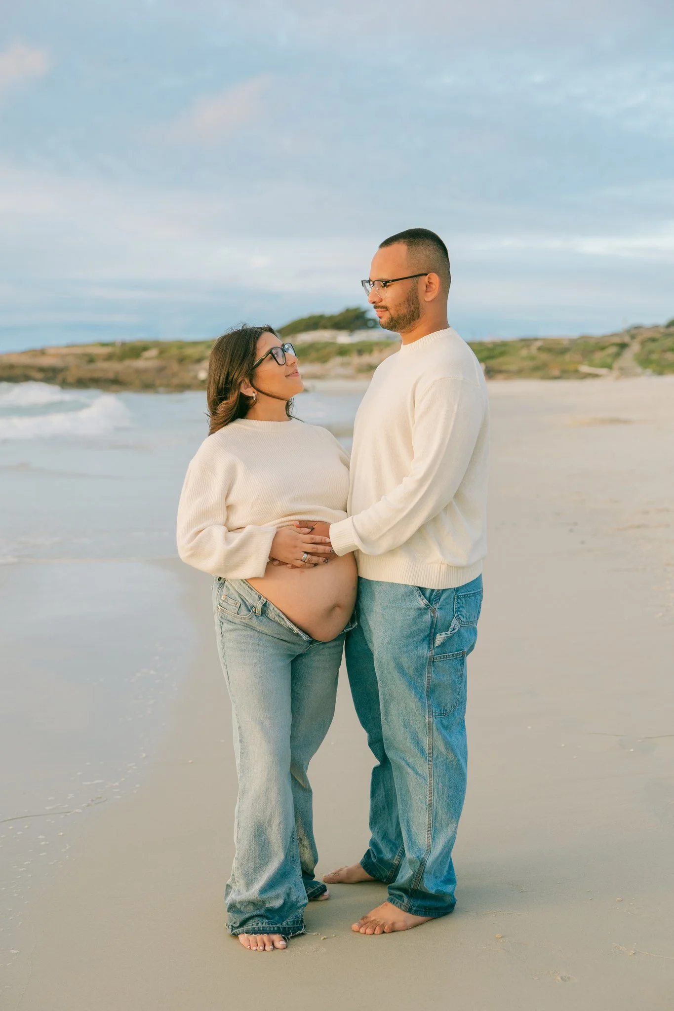 Couple embracing, looking at each other on the sandy beach posing for maternity portraits in Tampa, FL.