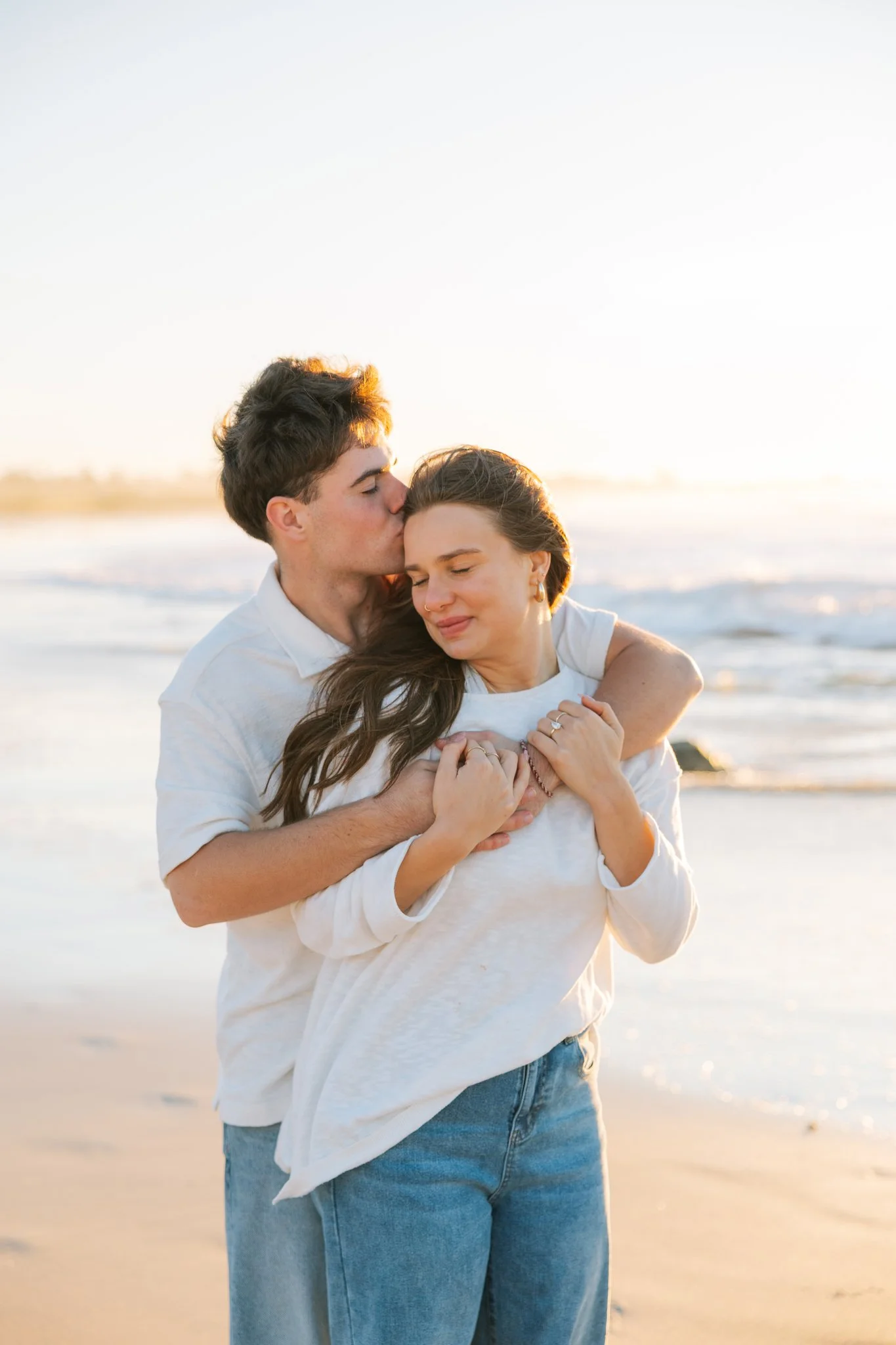 Couple embracing on the beach as the male kisses the forehead of the female during at Tampa, FL engagement session.