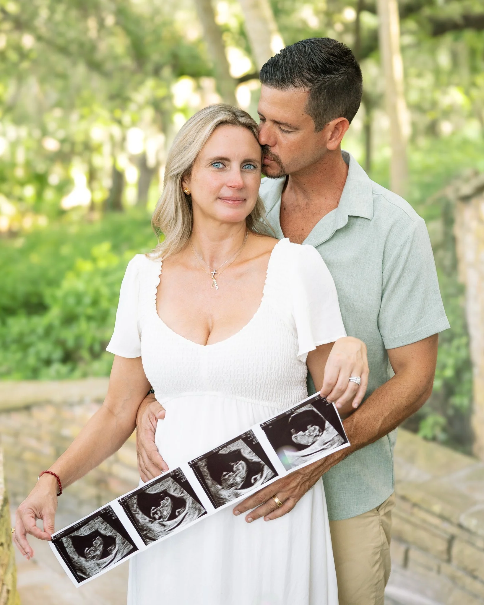 Close portrait of an expecting couple with an ultrasound strip, framed by green oaks in Safety Harbor