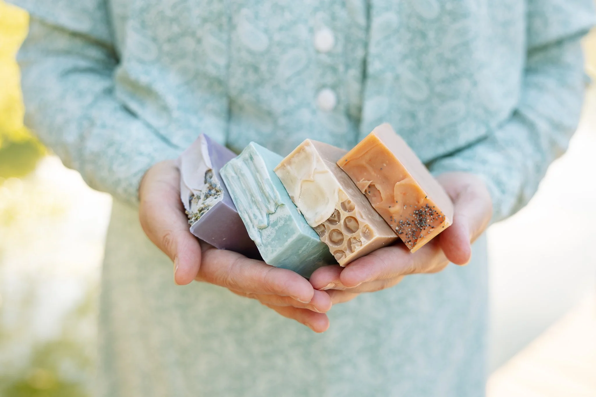 Soap maker holding four handmade Laurel Creek Soaps bars in lavender, blue, honeycomb, and orange poppy seed