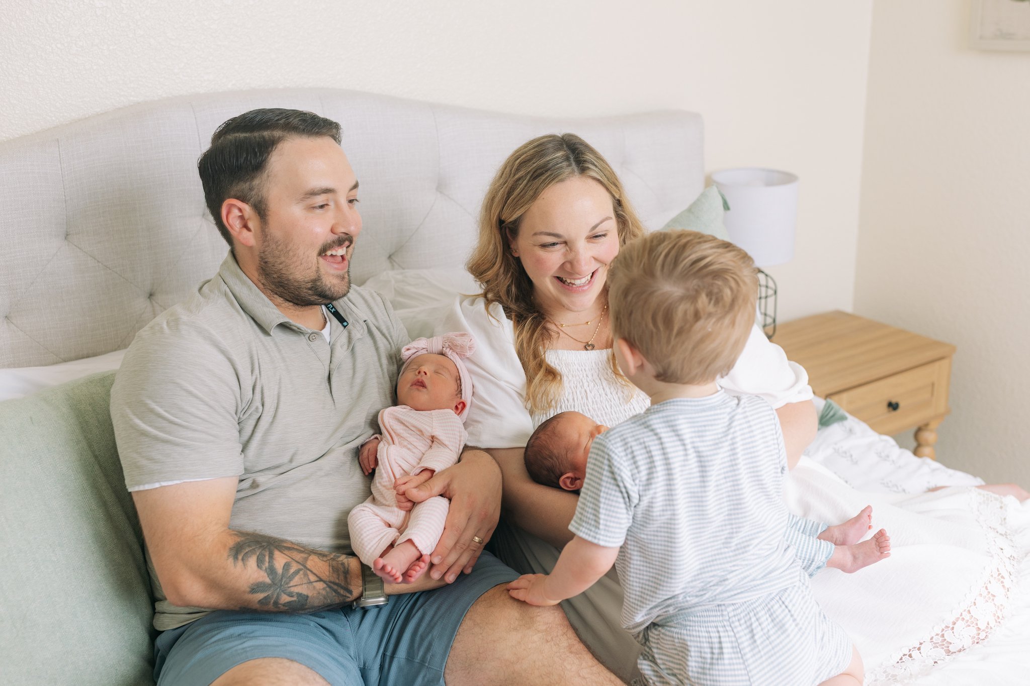 A mother and father holding their newborn twins while their toddler climbs onto the bed to join them during an at-home family session in Tampa, FL.