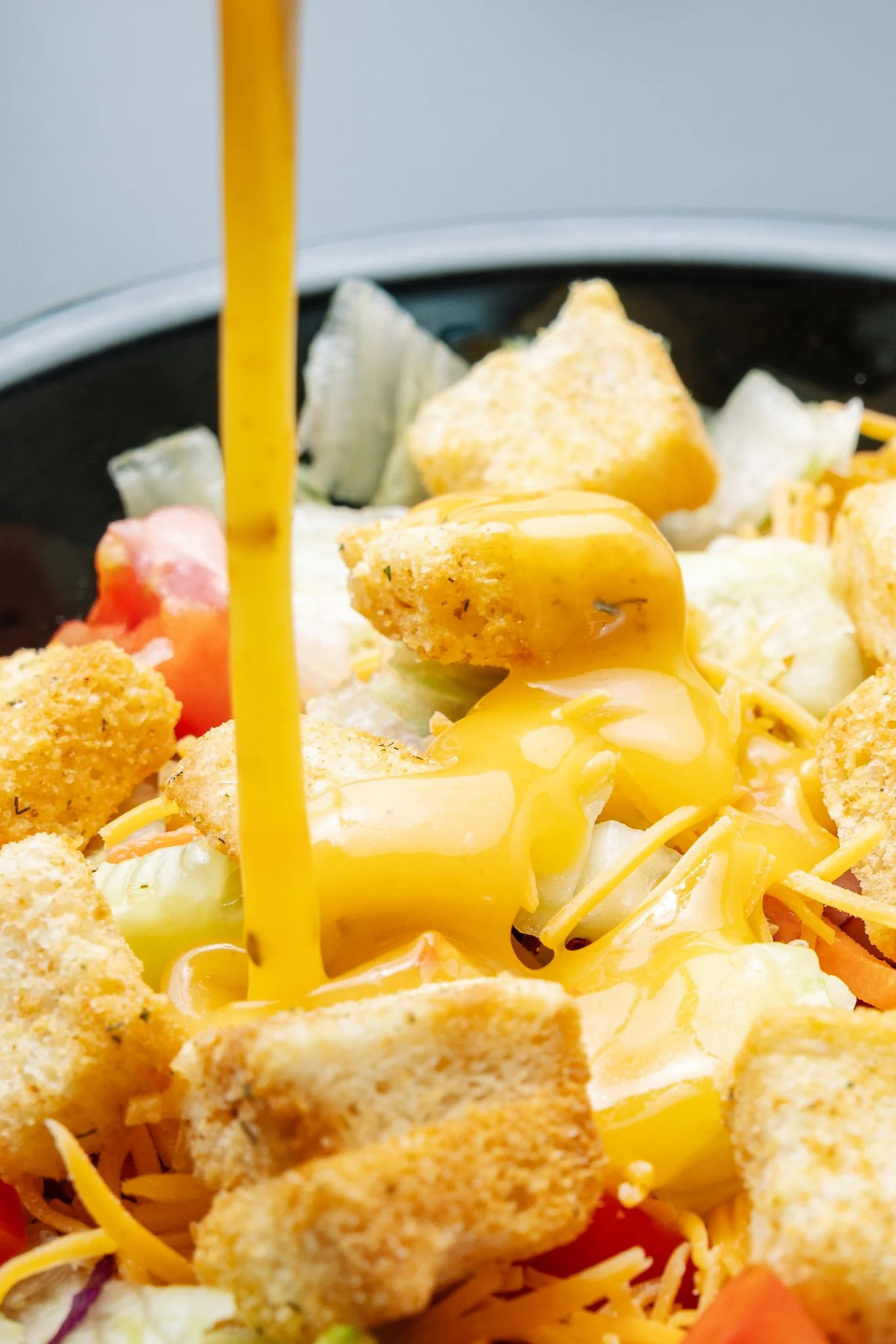 Close-up of a plate with fried chicken pieces, shredded cheese, and vegetables, with yellow liquid pouring over the food.