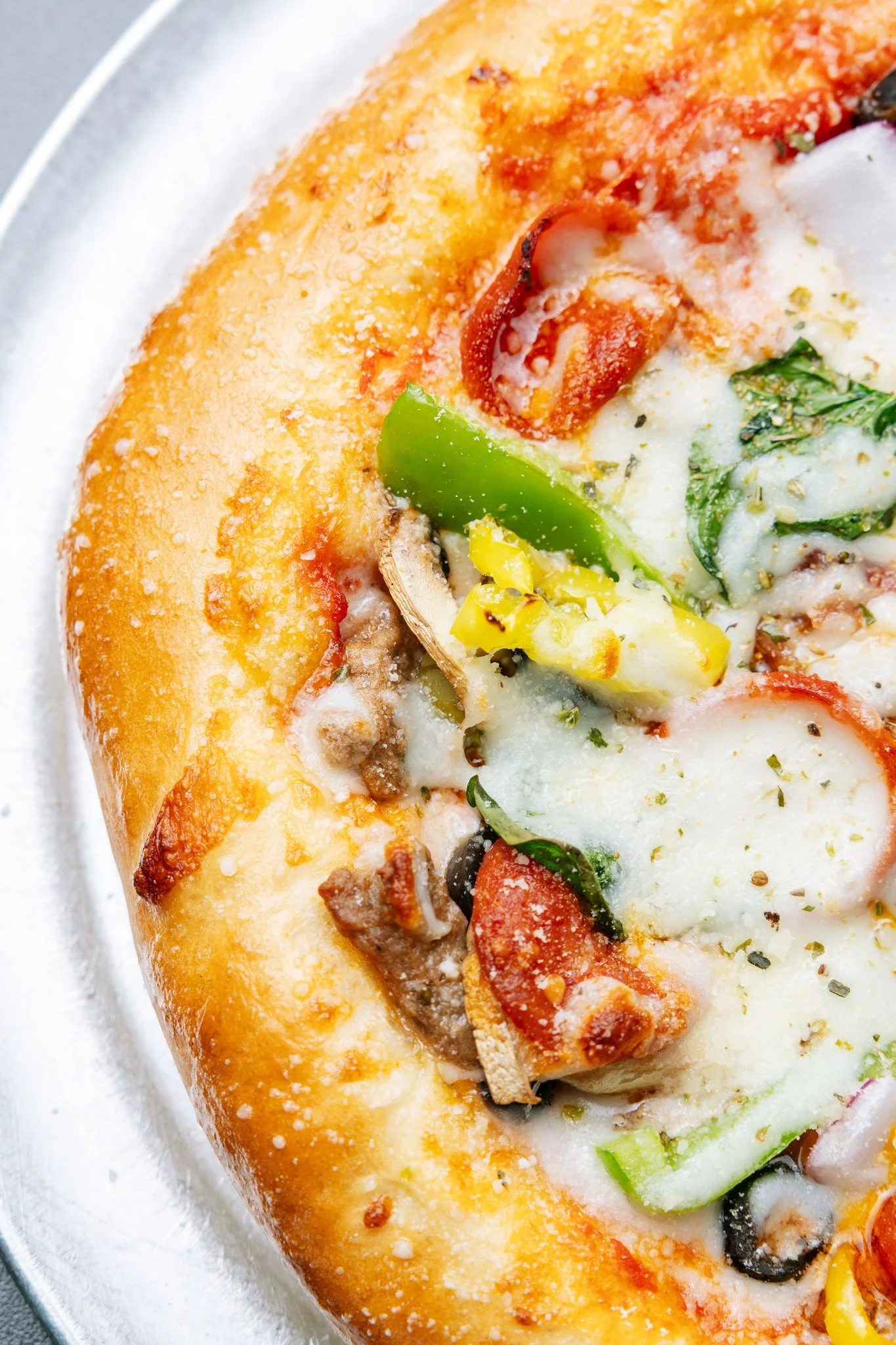 A close-up of a pizza with cheese, pepperoni, green peppers, black olives, mushrooms, and herbs.
