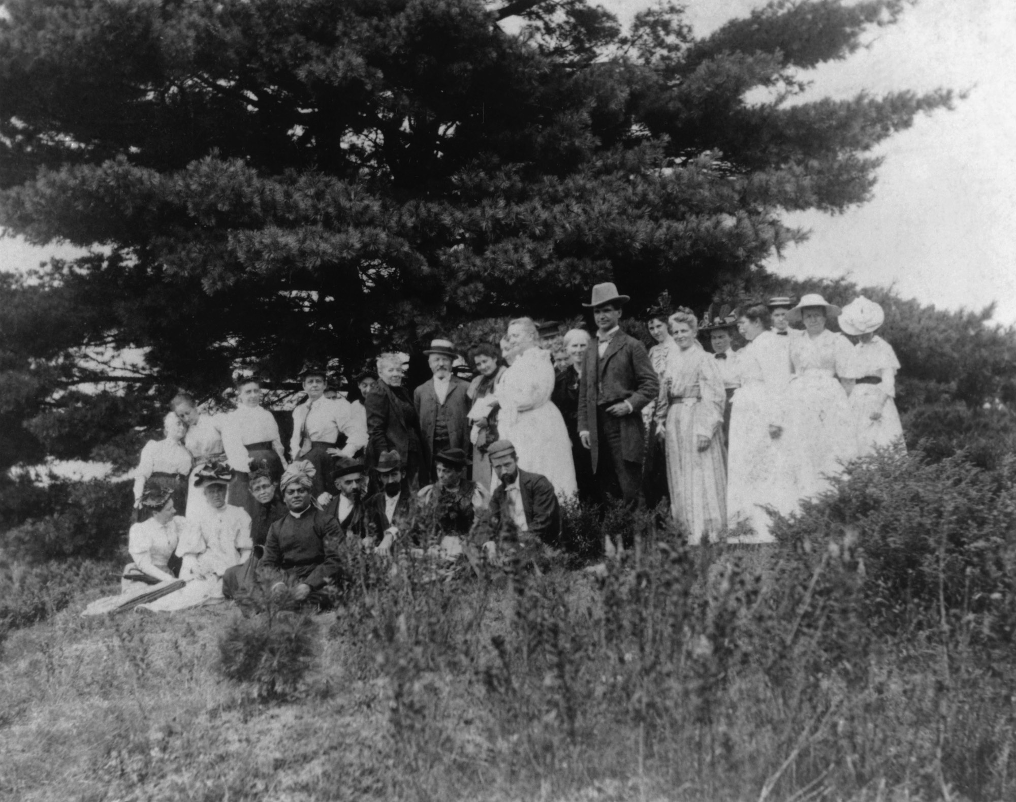 (#30) Green Acre, August 1894. Swamiji is seated under the “Swami’s Pine” at Green Acre, Maine. This picture of the group under the tree was taken by Cora Stockham.