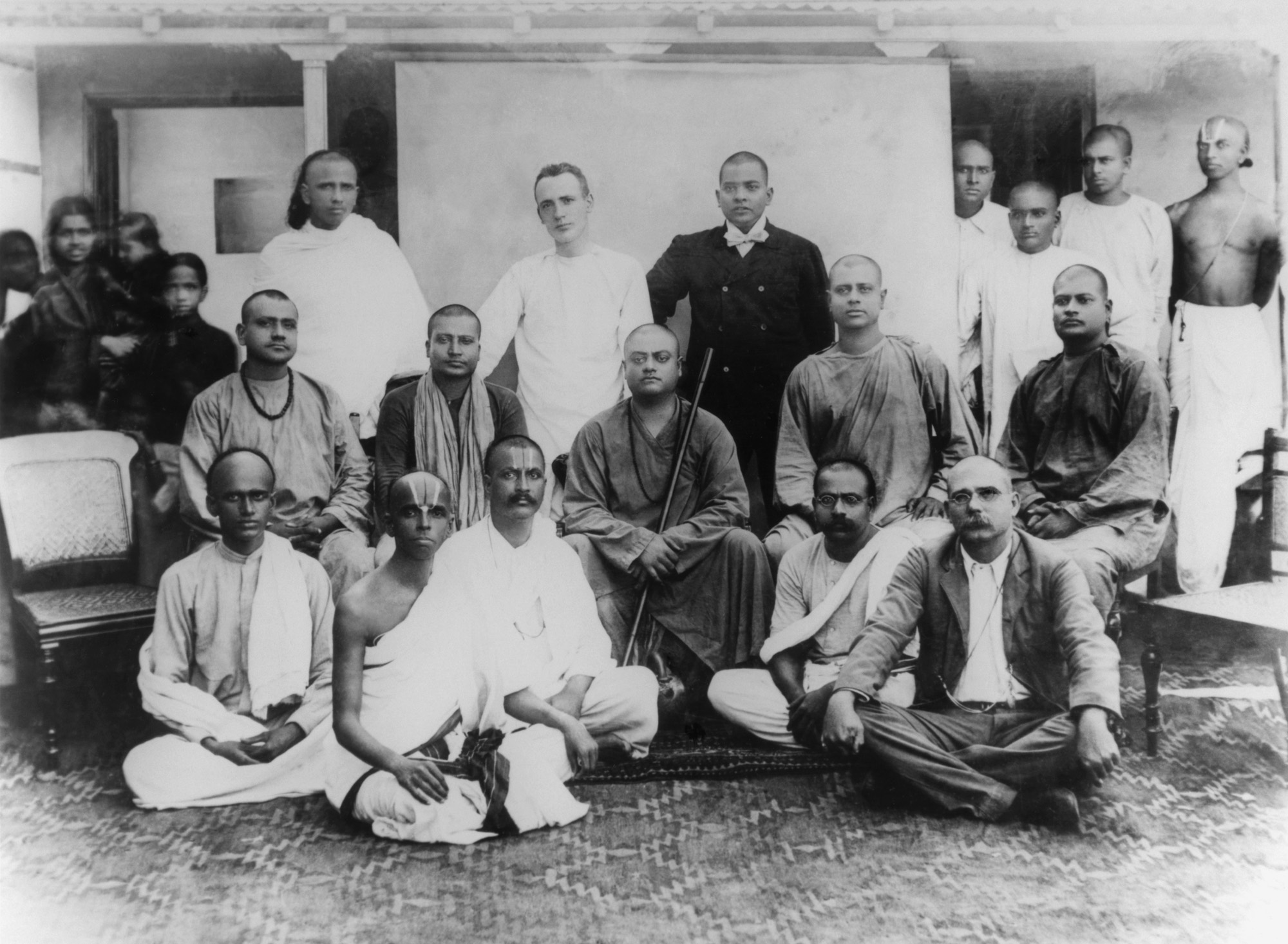 (#57) Chennai, February 1897. Sitting on chair ( from L): Tarapada (a monk from another Order), Swami Shivananda, Swamiji, Swami Niranjanananda, Swami Sadananda. Standing ( from L): Alasinga Perumal, J. J. Goodwin, M. N. Banerjee, and other devotees. Sitting ( from L): (second) Biligiri Iyengar, (fourth) M. C. Nanjunda Rao.