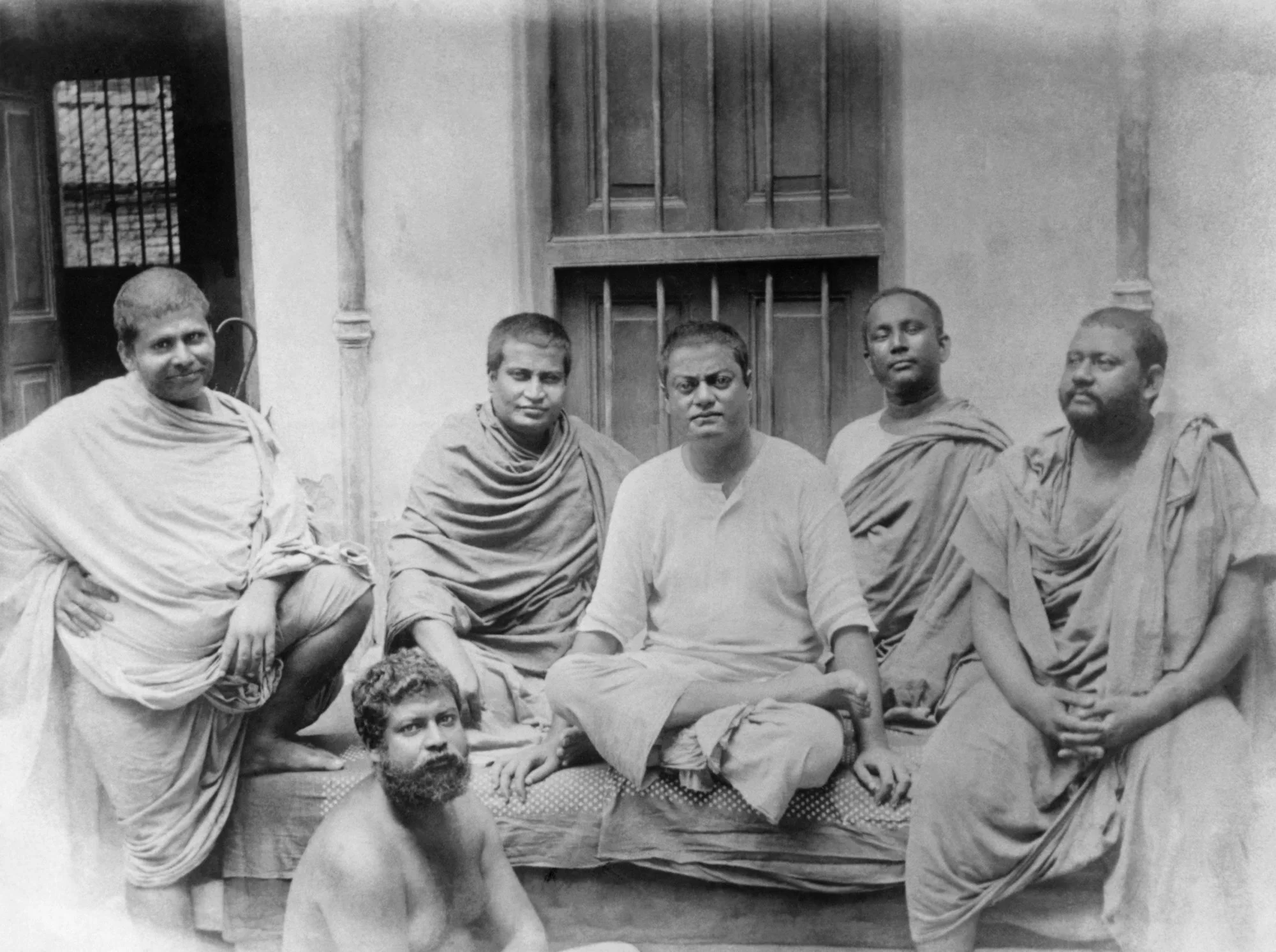 (#75) Kolkata, (June 20?), 1899. This picture was taken at a rented house (8 Bosepara Lane, where Holy Mother was staying at the time. ( From L): Swami Trigunatita, Swami Shivananda, Swamiji, Swami Turiyananda, Swami Brahmananda, and ( seated below ) Swami Sadananda.