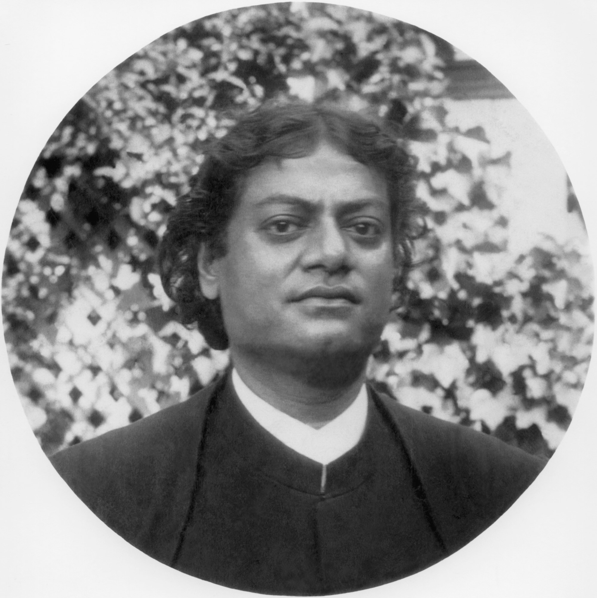 (#96) San Francisco, California. 1900. Swamiji was invited for lunch at the home of Charles Neilson. After lunch Swamiji stretched out on the lawn in the garden. Wishing to take Swamiji’s picture, Neilson requested him to pose. Swamiji was loath to get up but he did, clearly none too pleased. In the background is a vine-covered lattice. Someone then said, “Oh Swami, please smile for us!” Swamiji did, when the second photograph (#97) was taken.