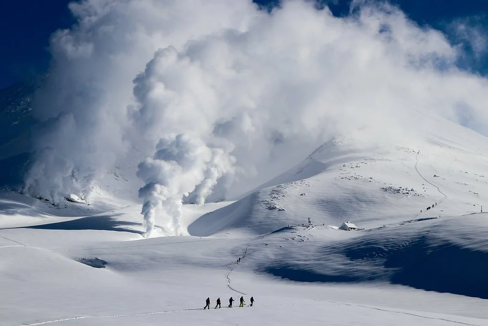 Group of Hokkaido Mountain Experiences Ski tourers and guide walking to the geothermal steam vents on Mount Asahidake on a sunny day.